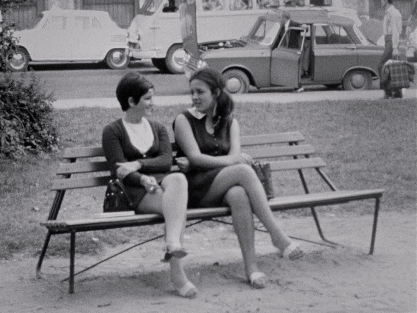 To unge kvinner sitter på en benk. Bildet er svarthvitt.