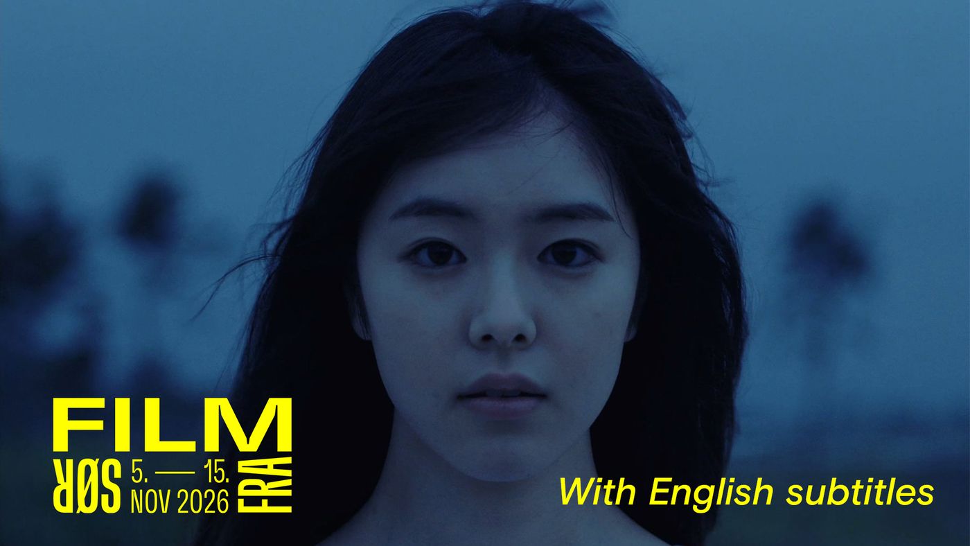 En ung kvinne med langt, moerkt haar som blafrer i vinden, ser mot kameraet i skumringen. Bakgrunnen er uklar.