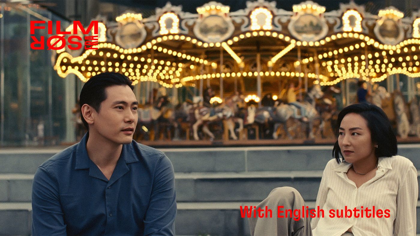 En mann og en kvinne sitter på trappetrinn foran en opplyst karusell.