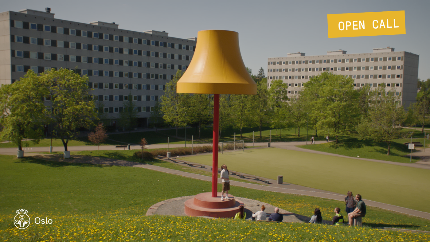 Noen mennesker står foran en kjempestor lampeskulptur. Blokker i bakgrunnen