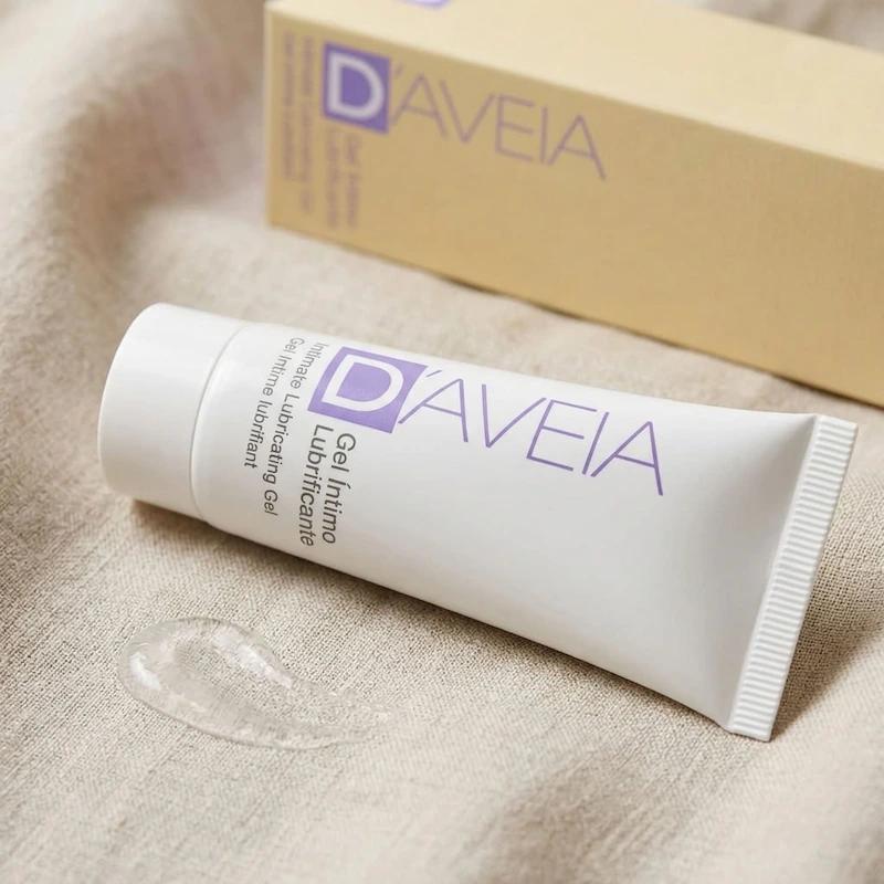 Weiße Tube D'AVEIA Intim-Gleitgel (Gel Íntimo Lubrificante) liegend auf hellem Stoff, mit einem Tropfen des transparenten Gels im Vordergrund und der Verpackung unscharf im Hintergrund.