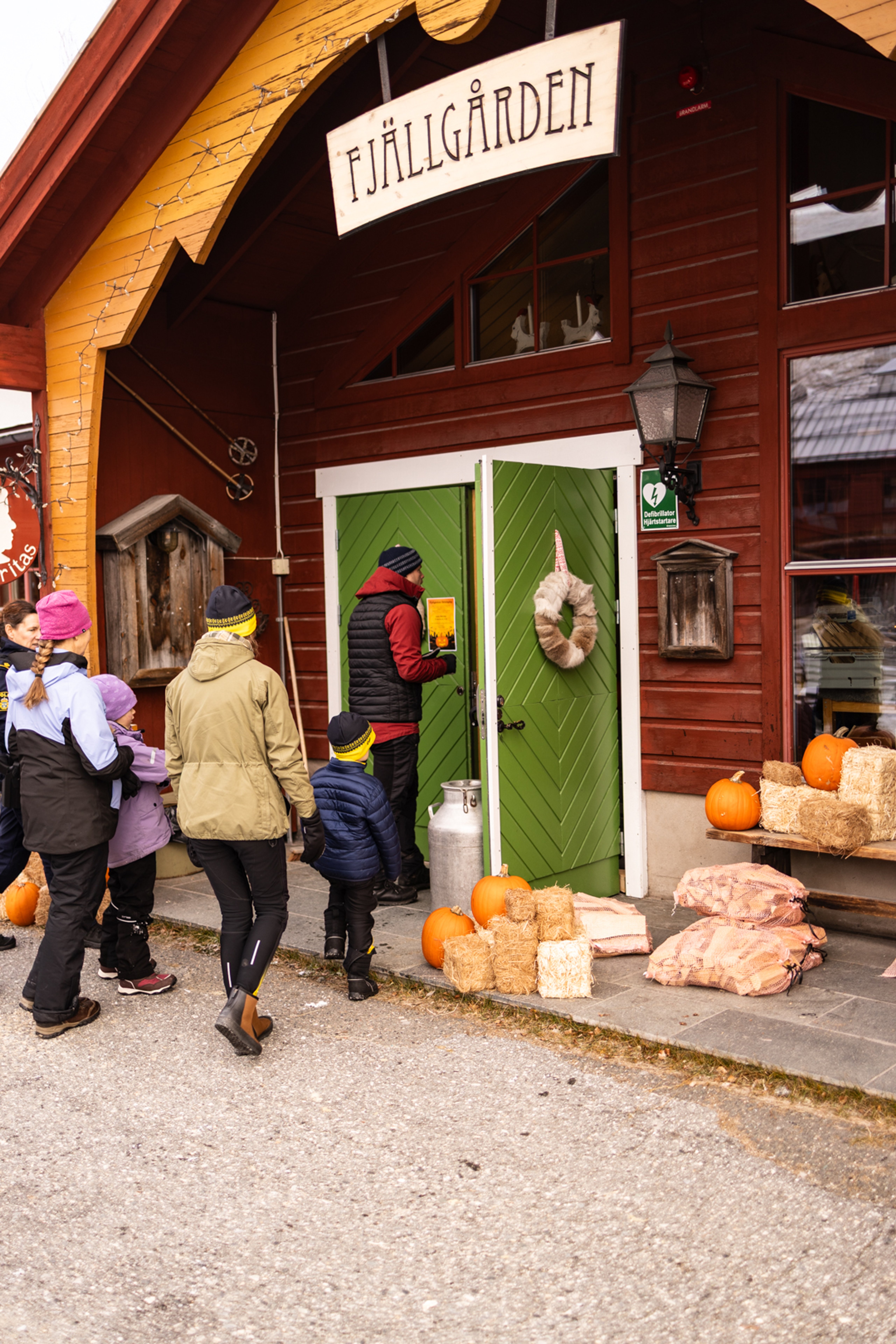 En grupp människor som står utanför en byggnad som är höstpyntad med pumpor och höbalar.