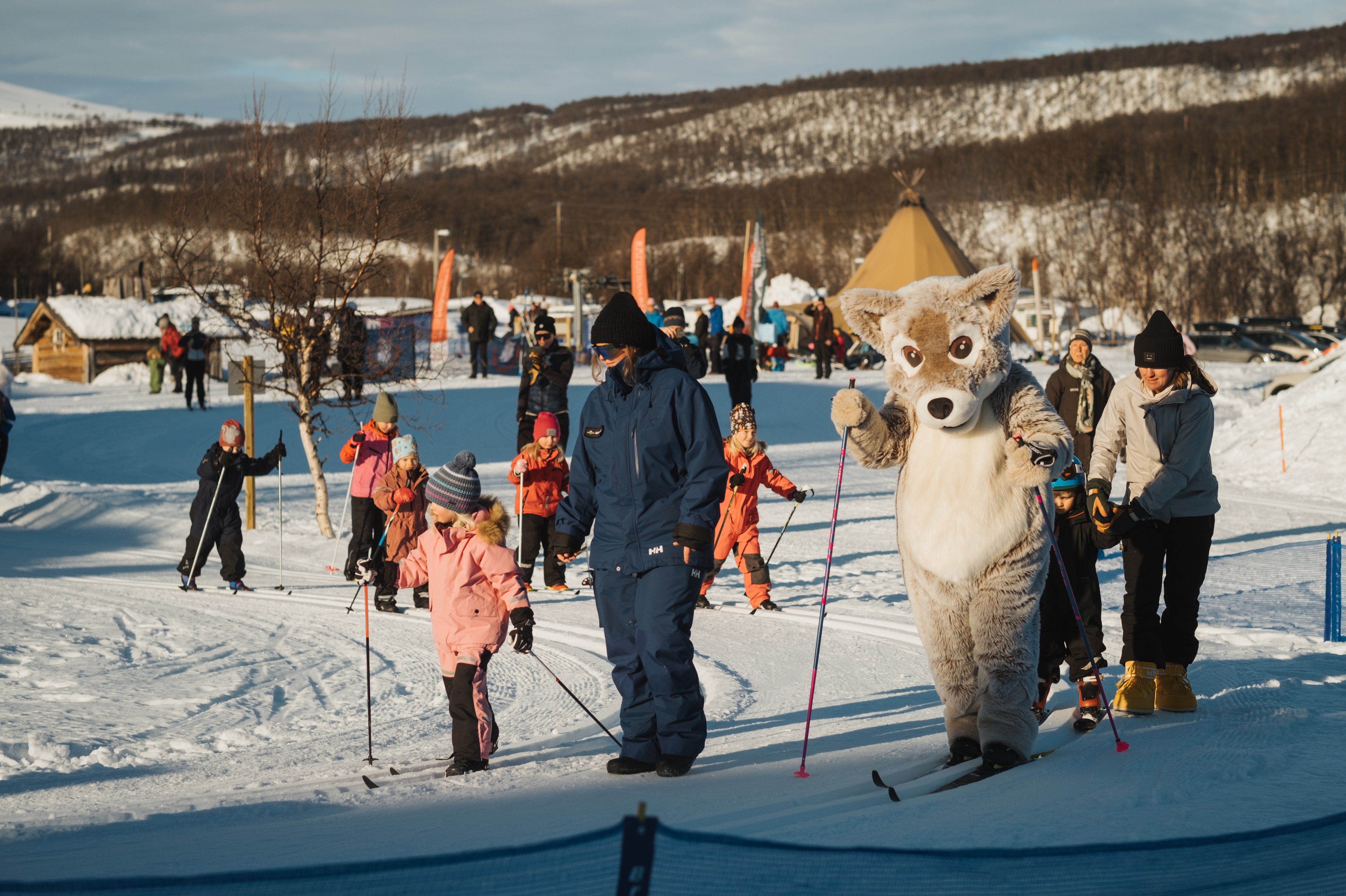 A group of children cross-country skiing with Mickelina the Arctic fox mascot.