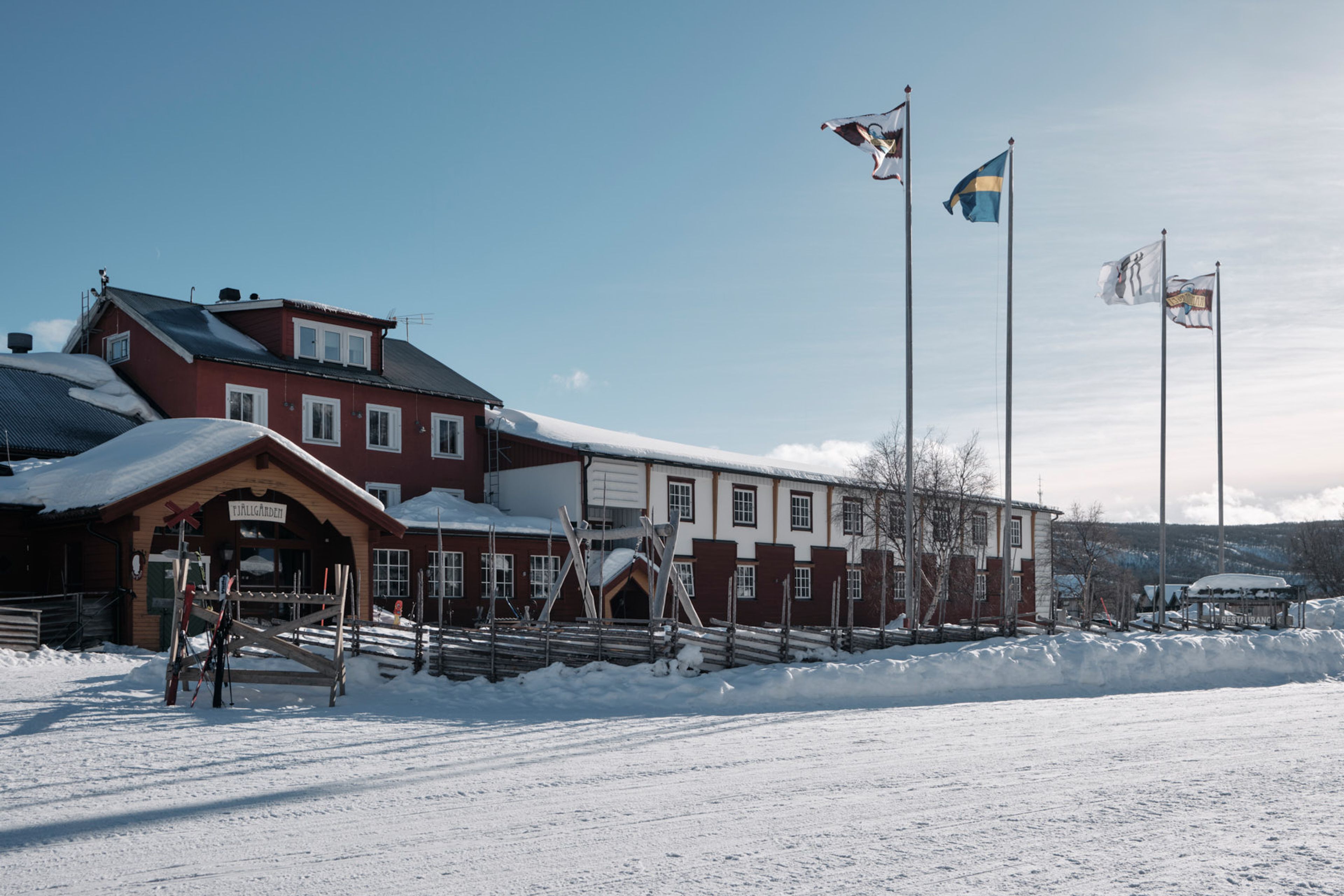 Ett rött fjällhotell med snötäckt gärdesgård runt om.