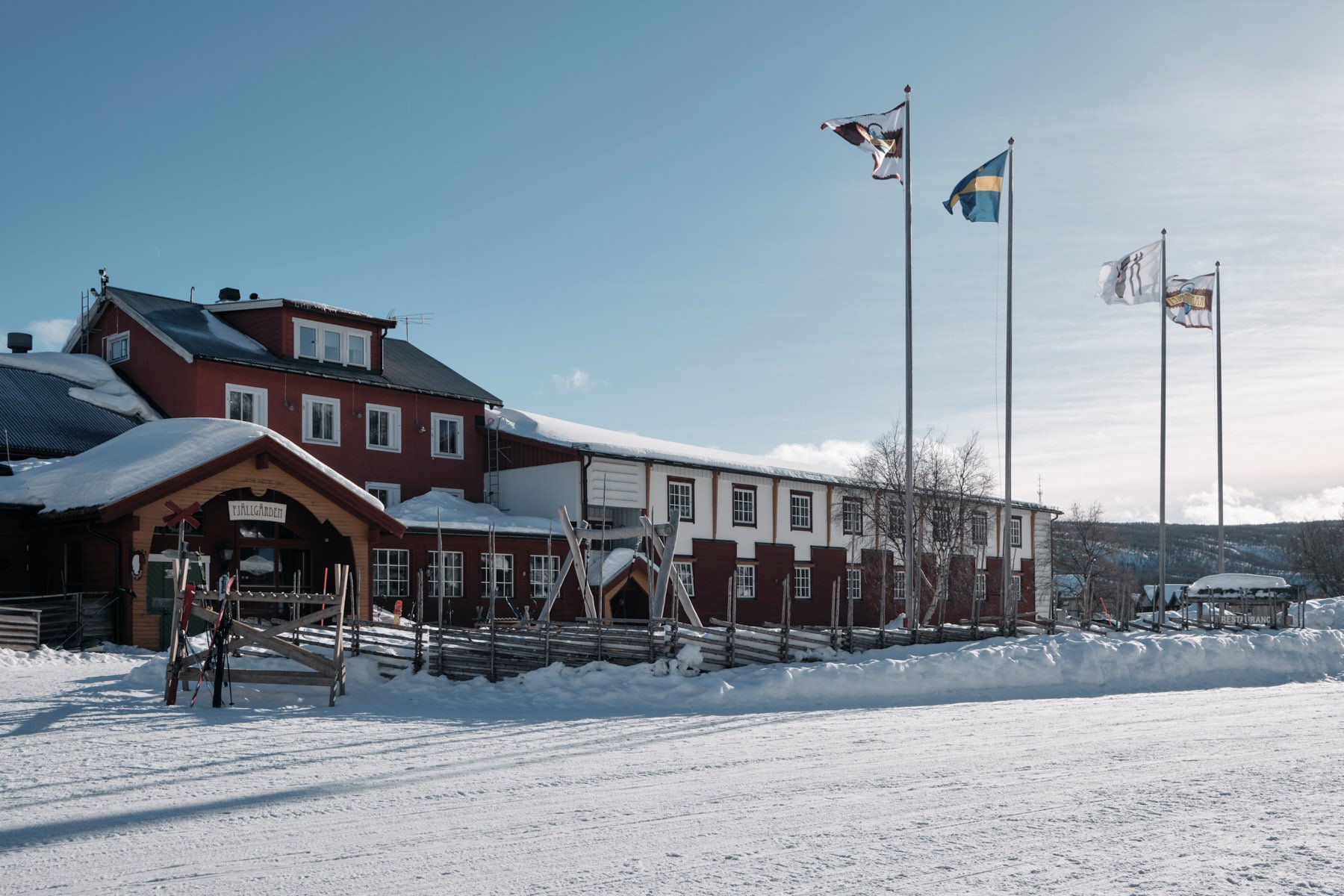 A red mountain hotel surrounded by a snow-covered traditional wooden fence.