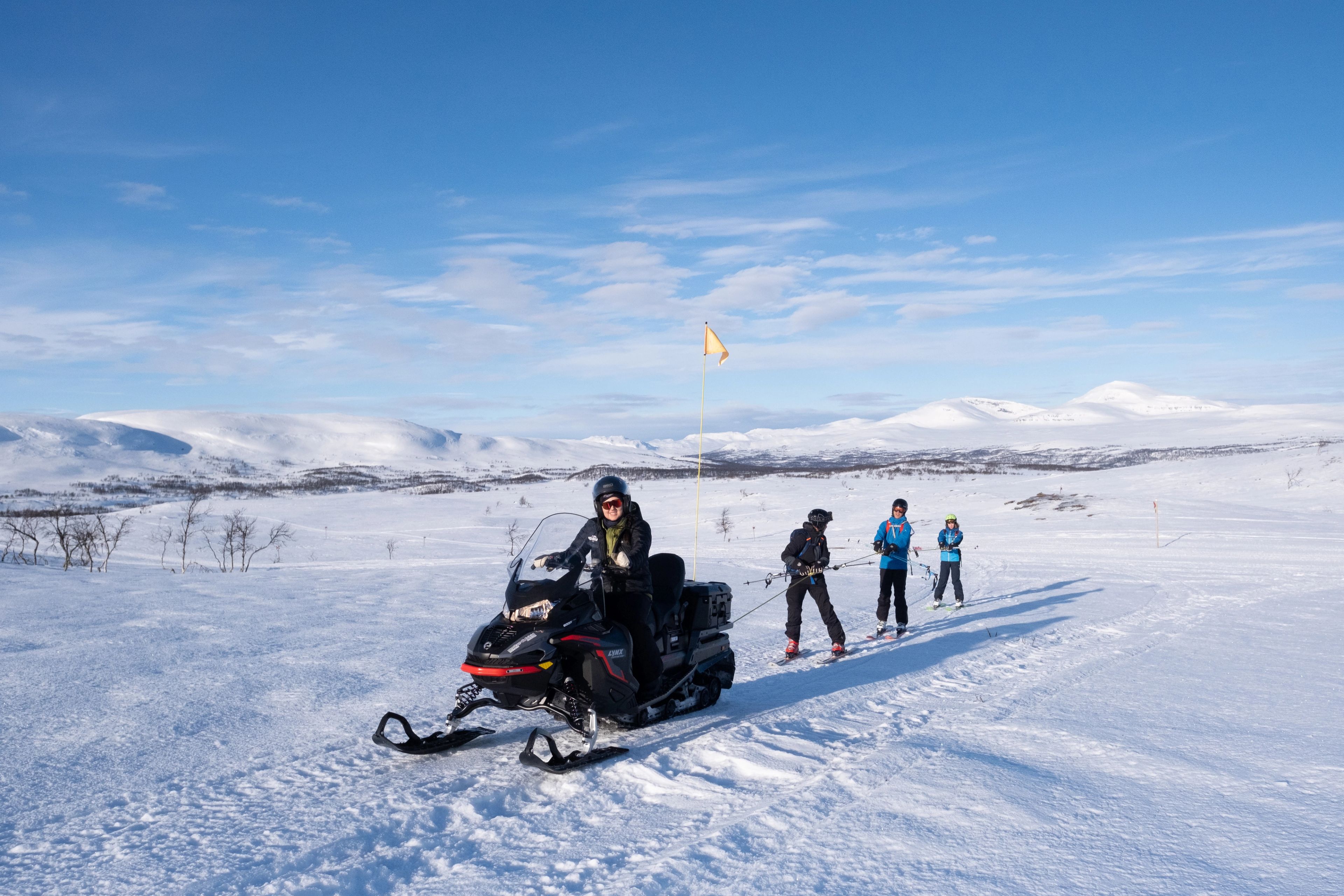En grupp människor tolkar på skidor bakom en snöskoter.