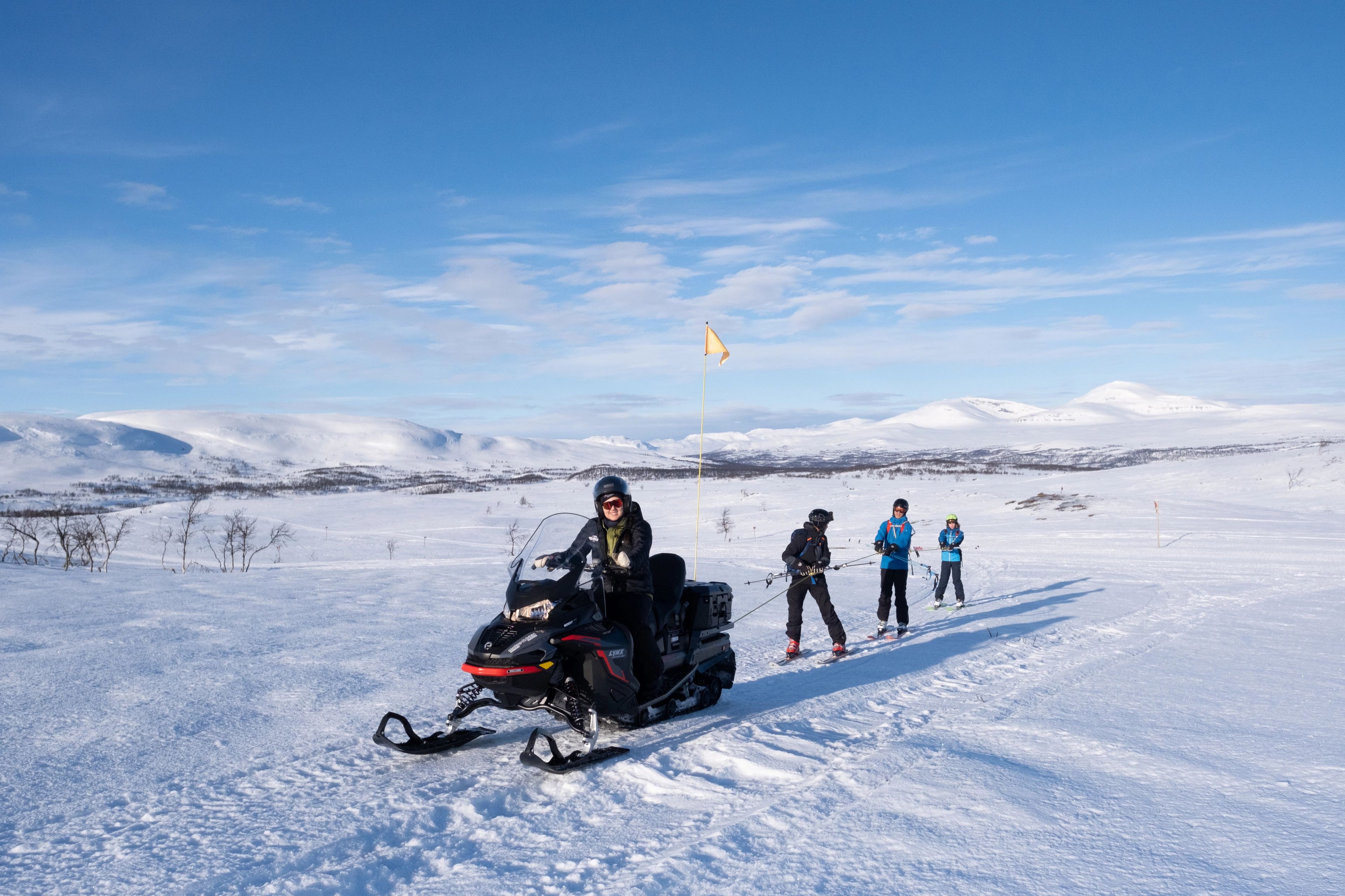 En grupp människor tolkar på skidor bakom en snöskoter.