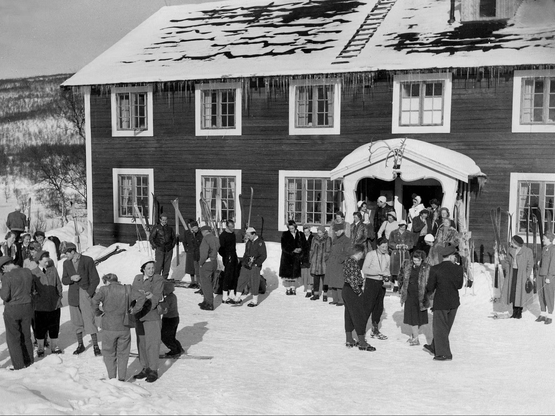 En gammal bild på en grupp människor som står framför ett fjällhotell.