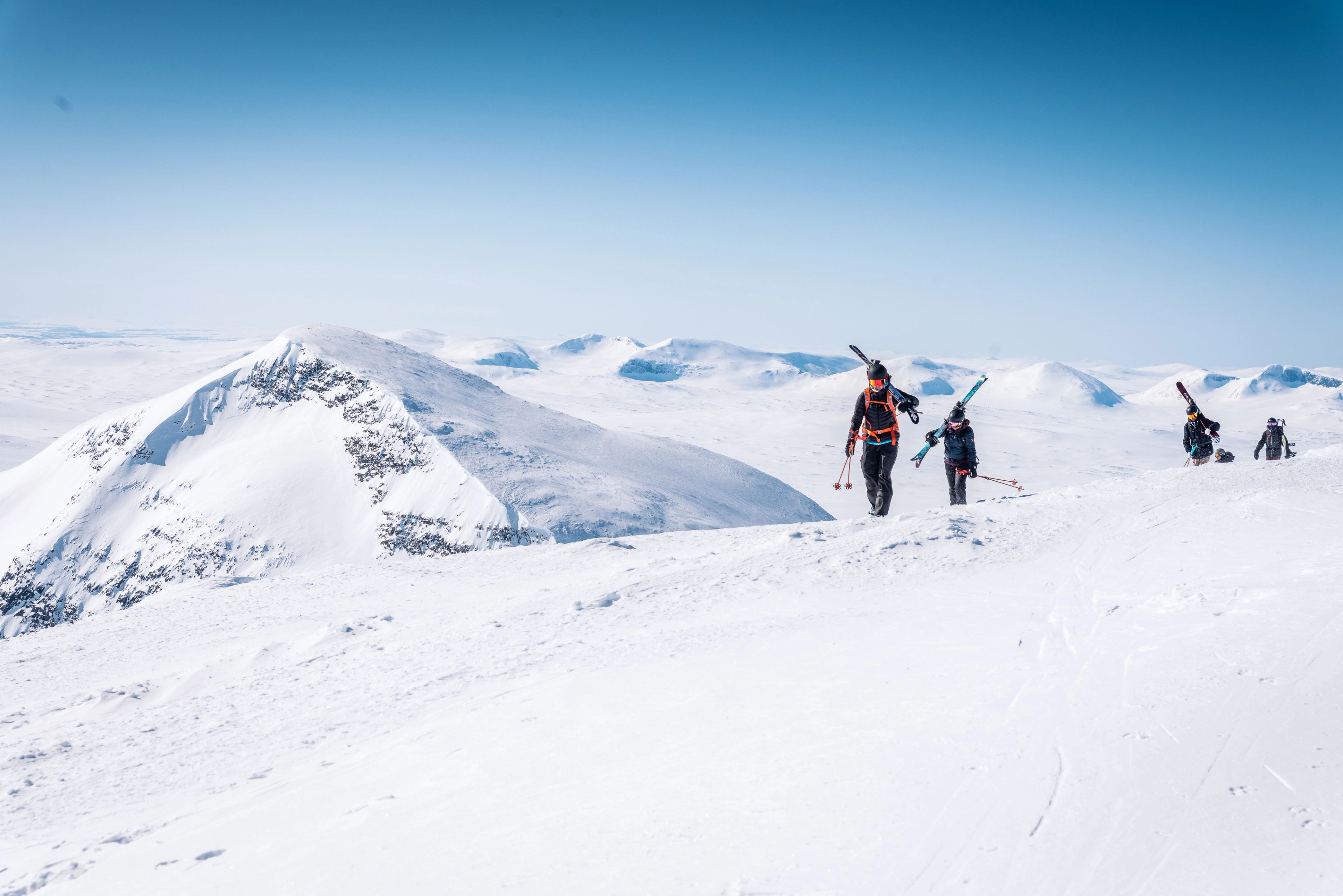 En grupp människor som går uppför en snötäckt sluttning med skidorna på ryggen.