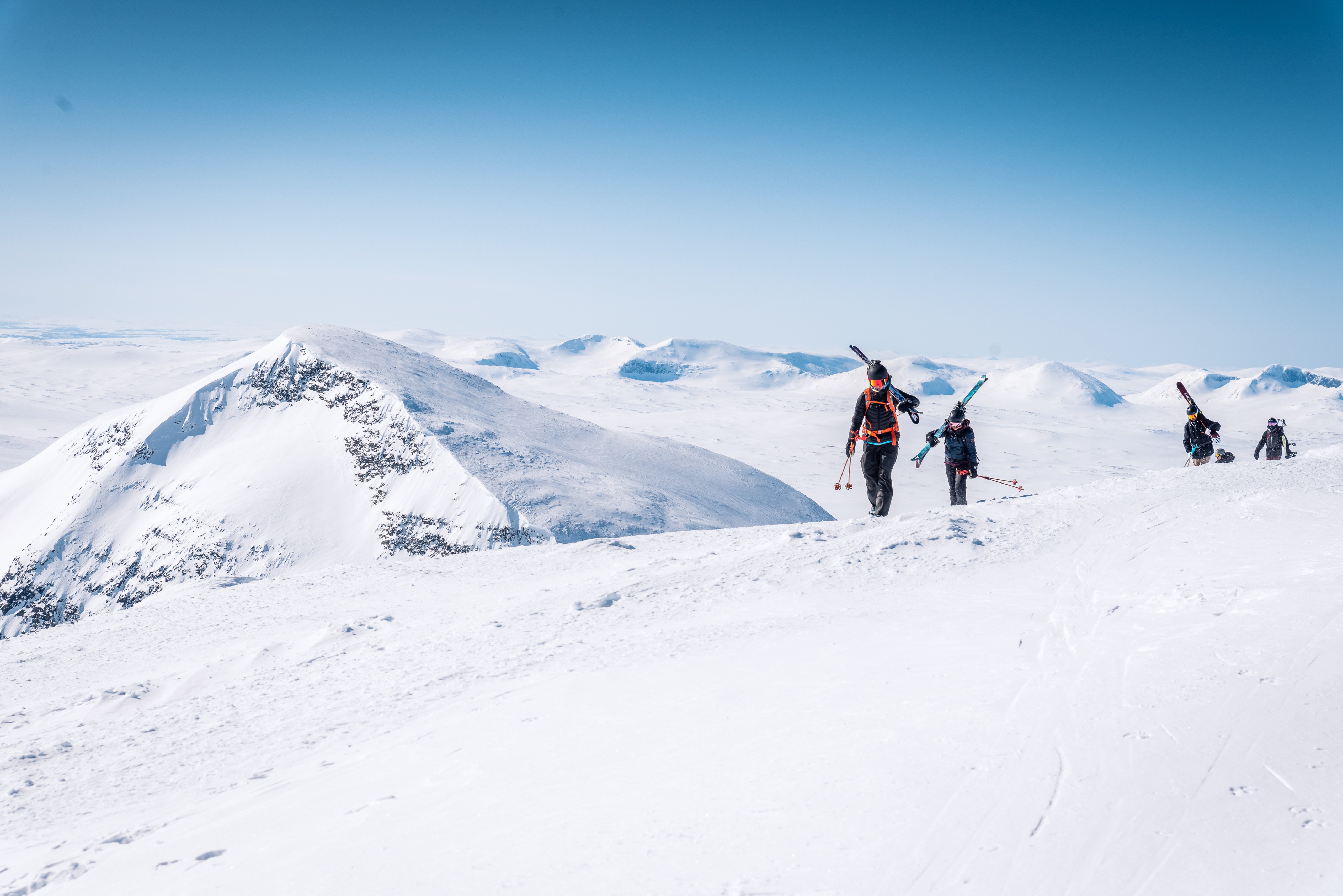A group of people walking up a snow-covered slope with skis on their backs.