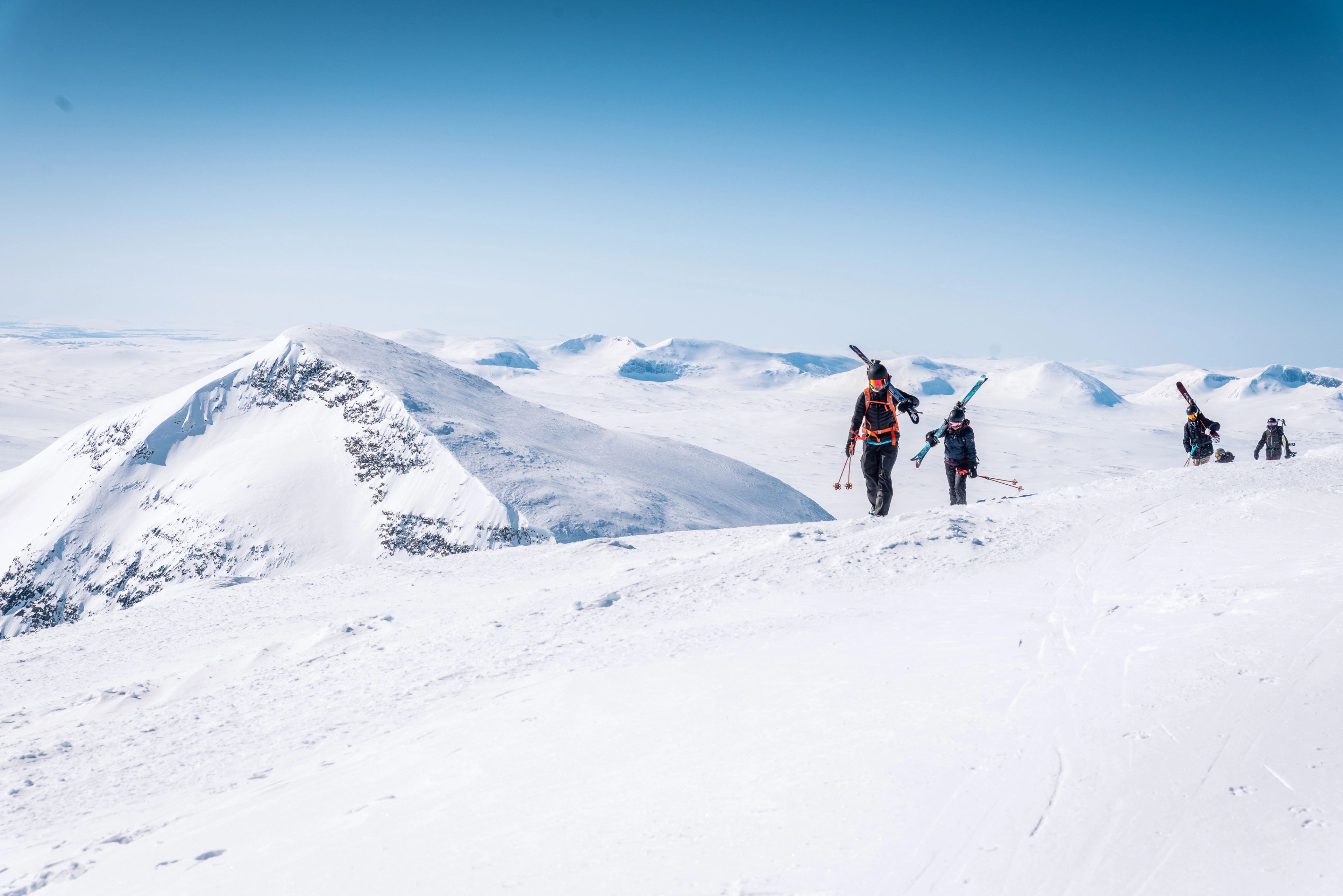 En grupp människor som går uppför en snötäckt sluttning med skidorna på ryggen.