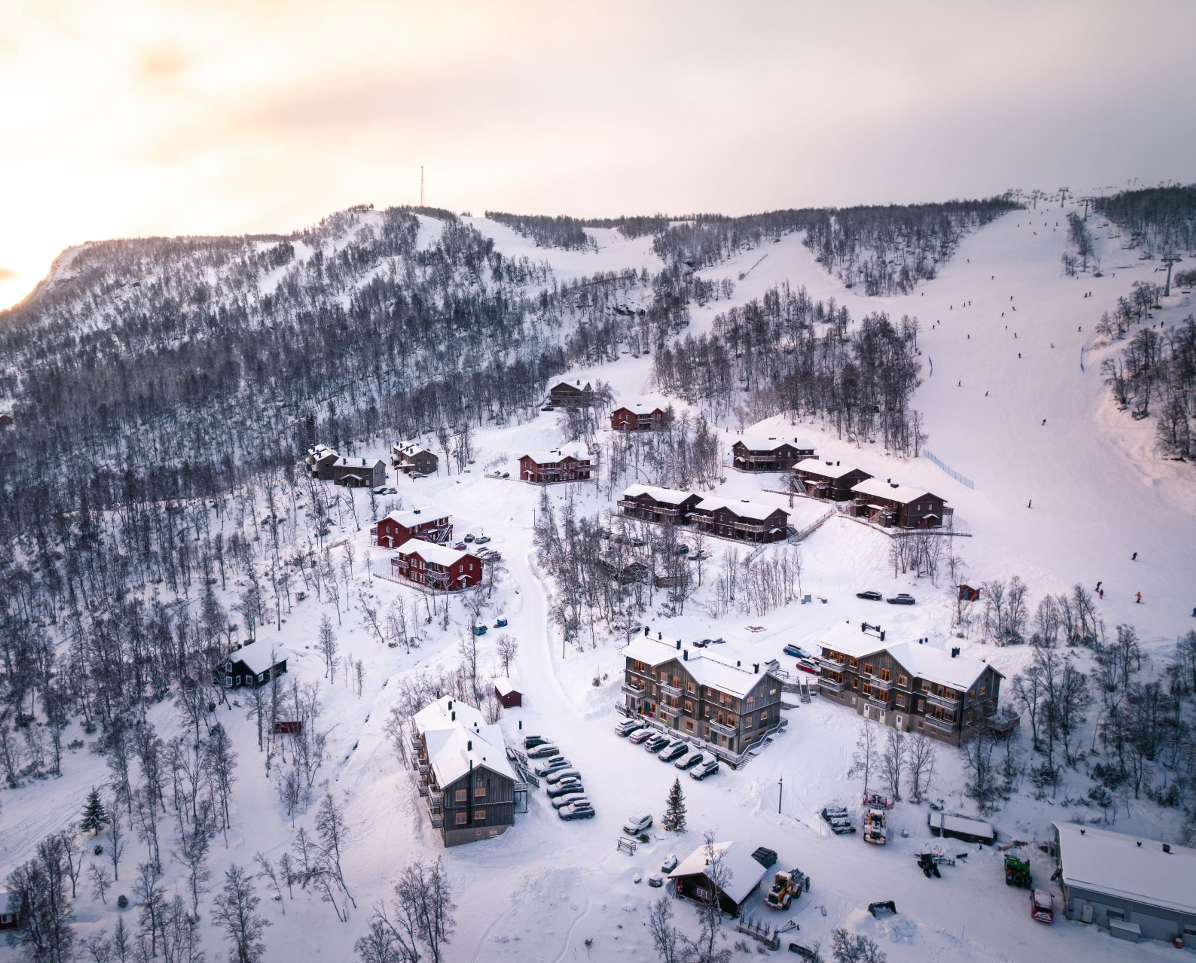 En drönarbild över ett boendeområde på en bergssluttning omgiven av skidbackar.