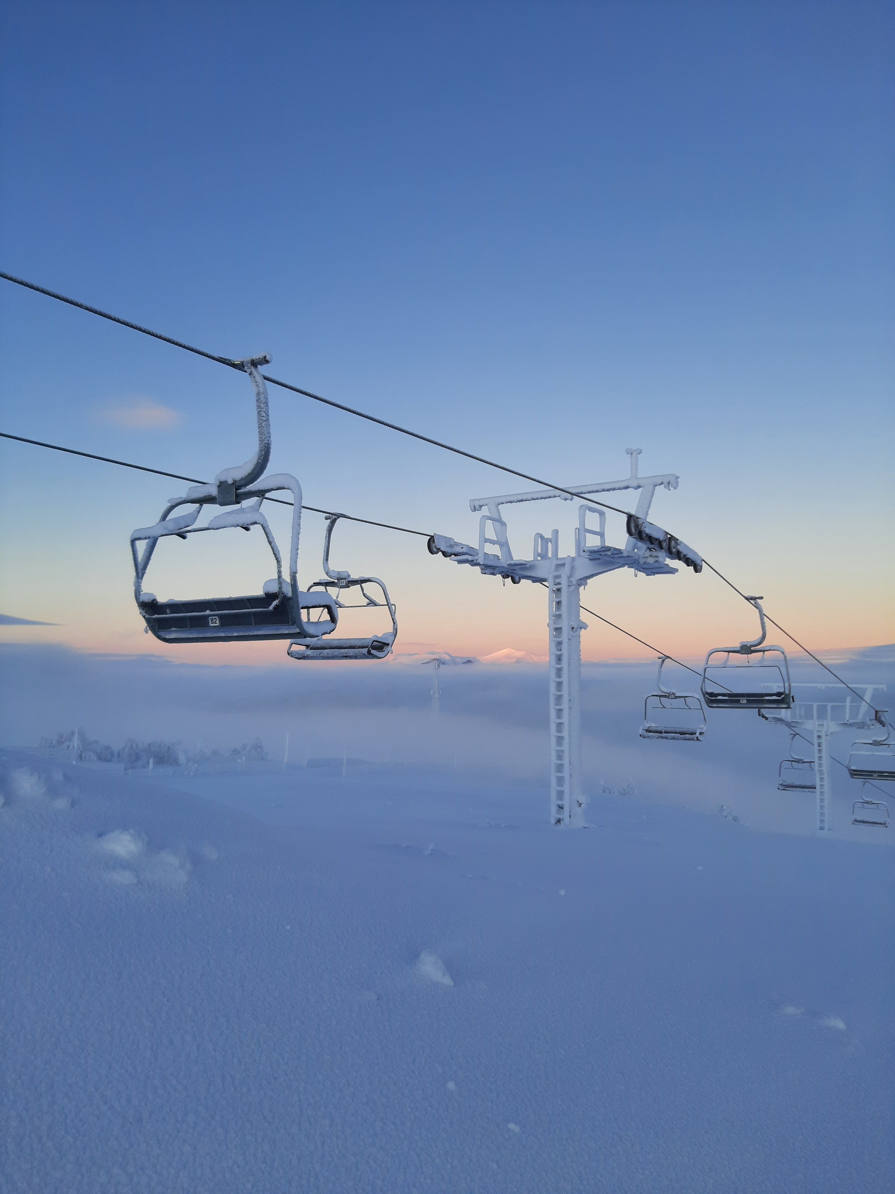 Frosty ski lifts on a snowy mountain under a gradient blue and orange sky.