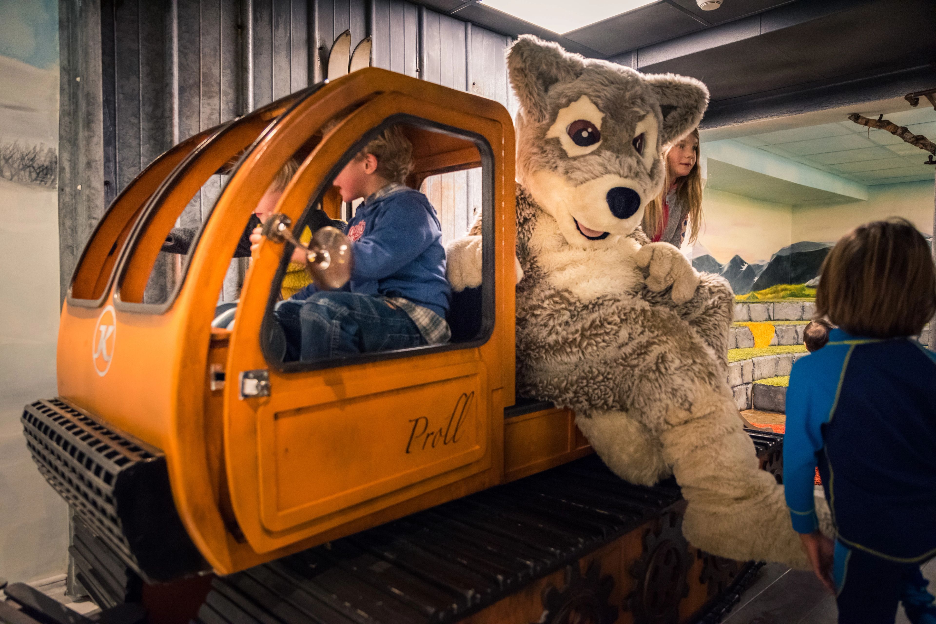 Maskoten Mickelina fjällräv åker på flaket på en miniatyrpistmaskin.