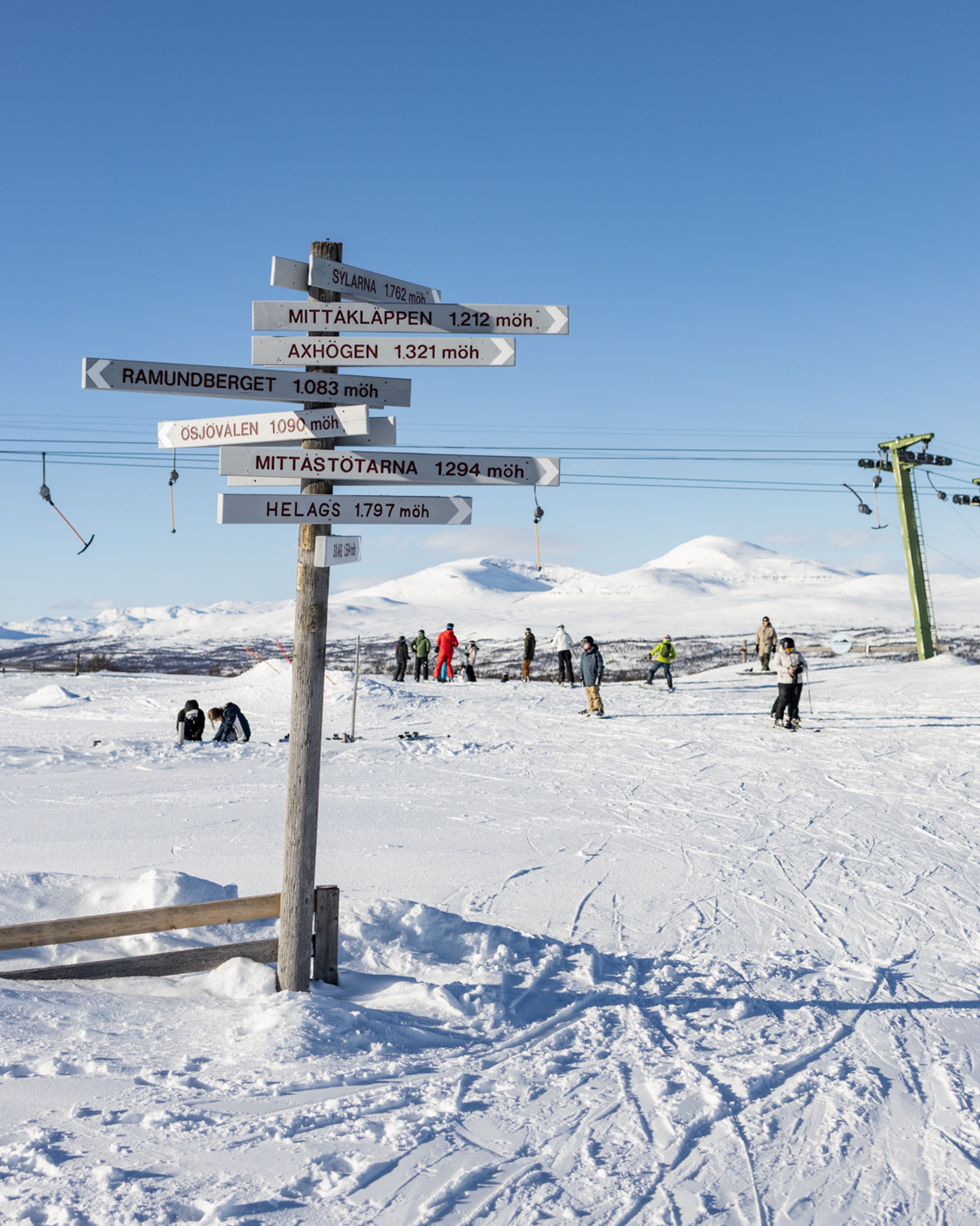 En grupp människor på toppen av en skidbacke med fjäll i bakgrunden.