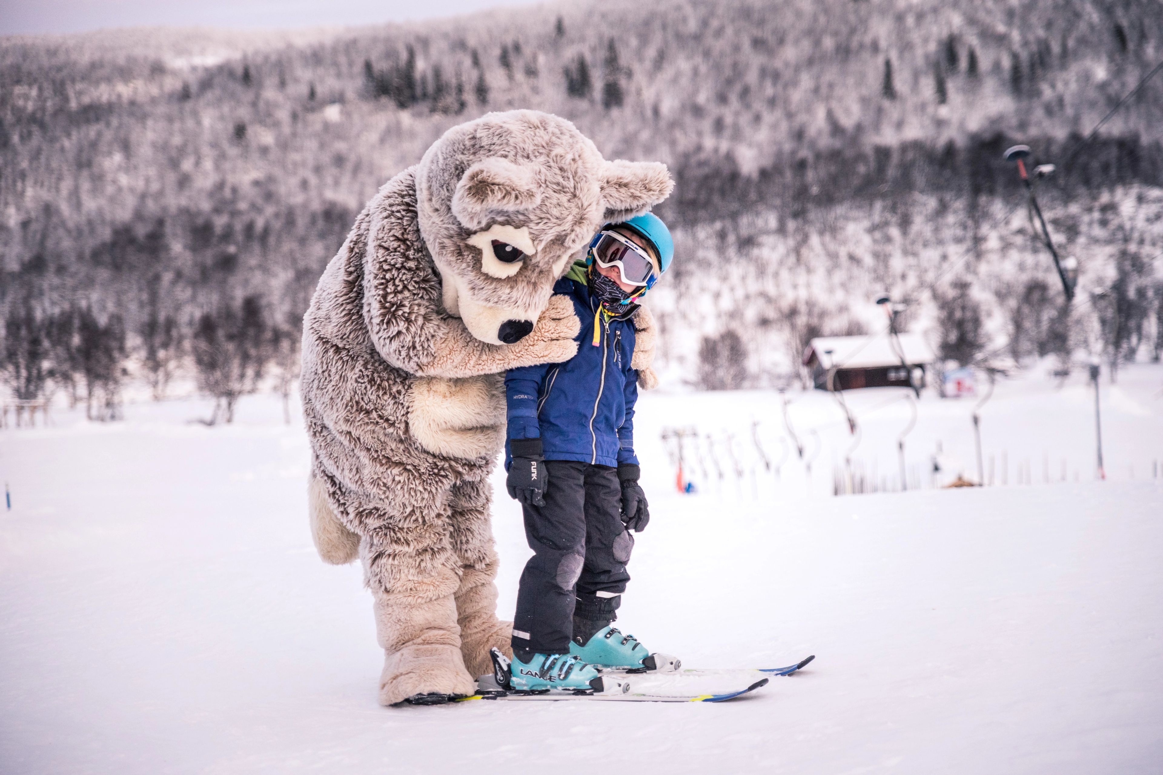 En liten pojke på skidor kramar maskoten fjällräven Mickelina.