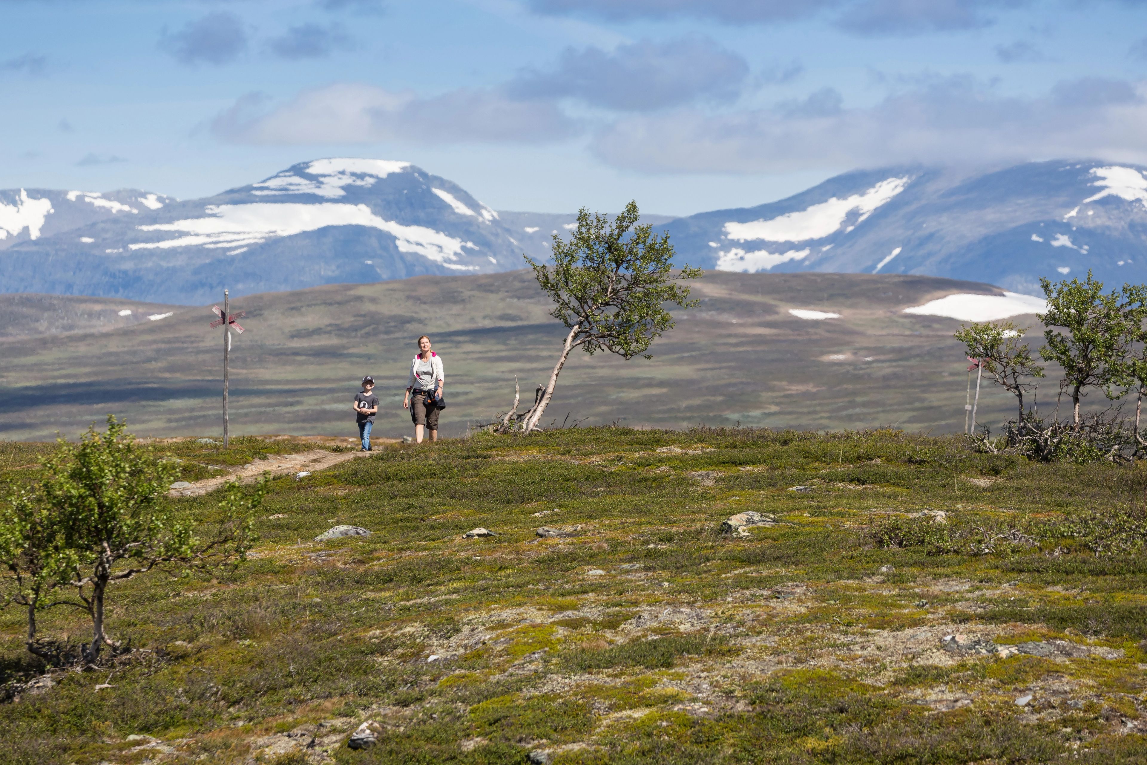 En kvinna och ett barn som går upp på en vandrinsled med fjäll i bakgrunden.
