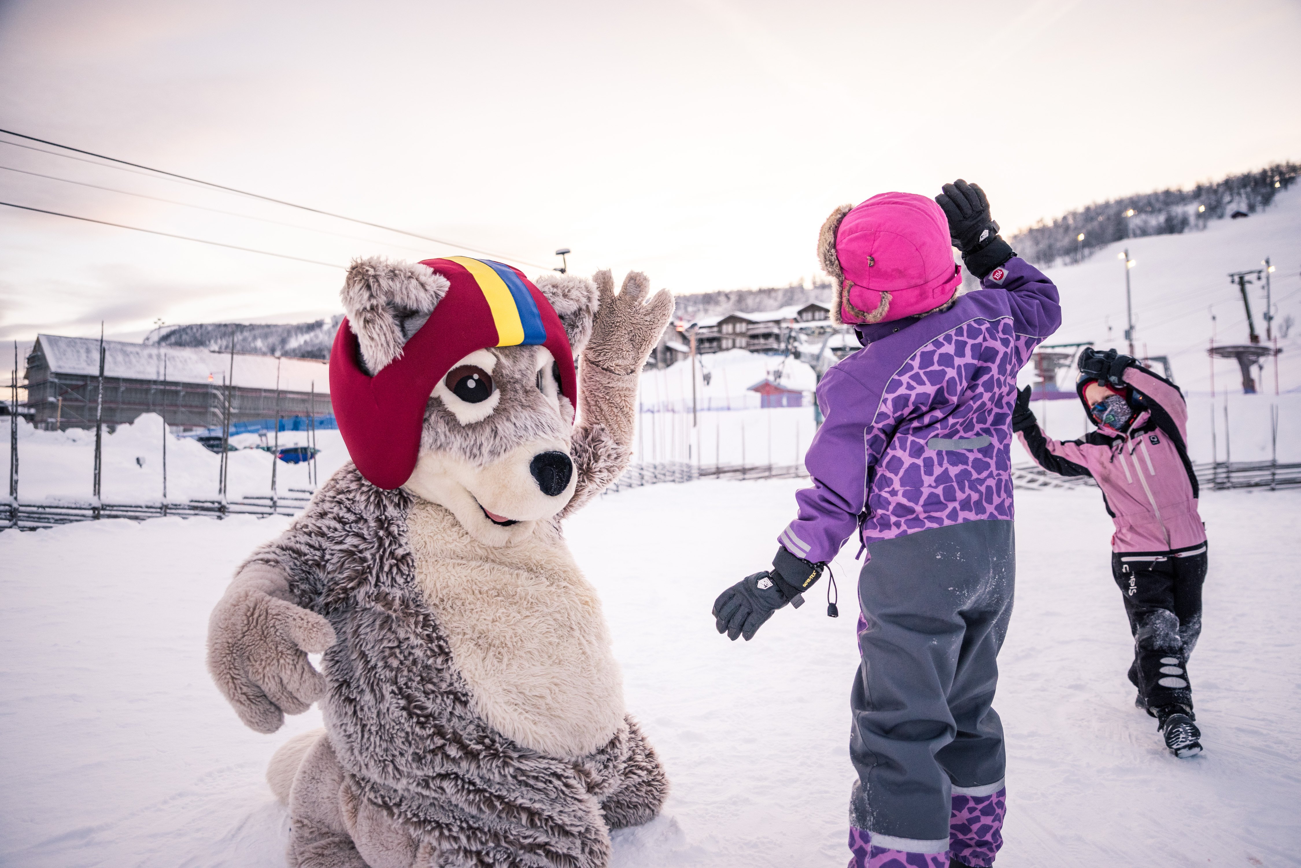 Two children play in the snow with Mickelina the Arctic fox mascot.