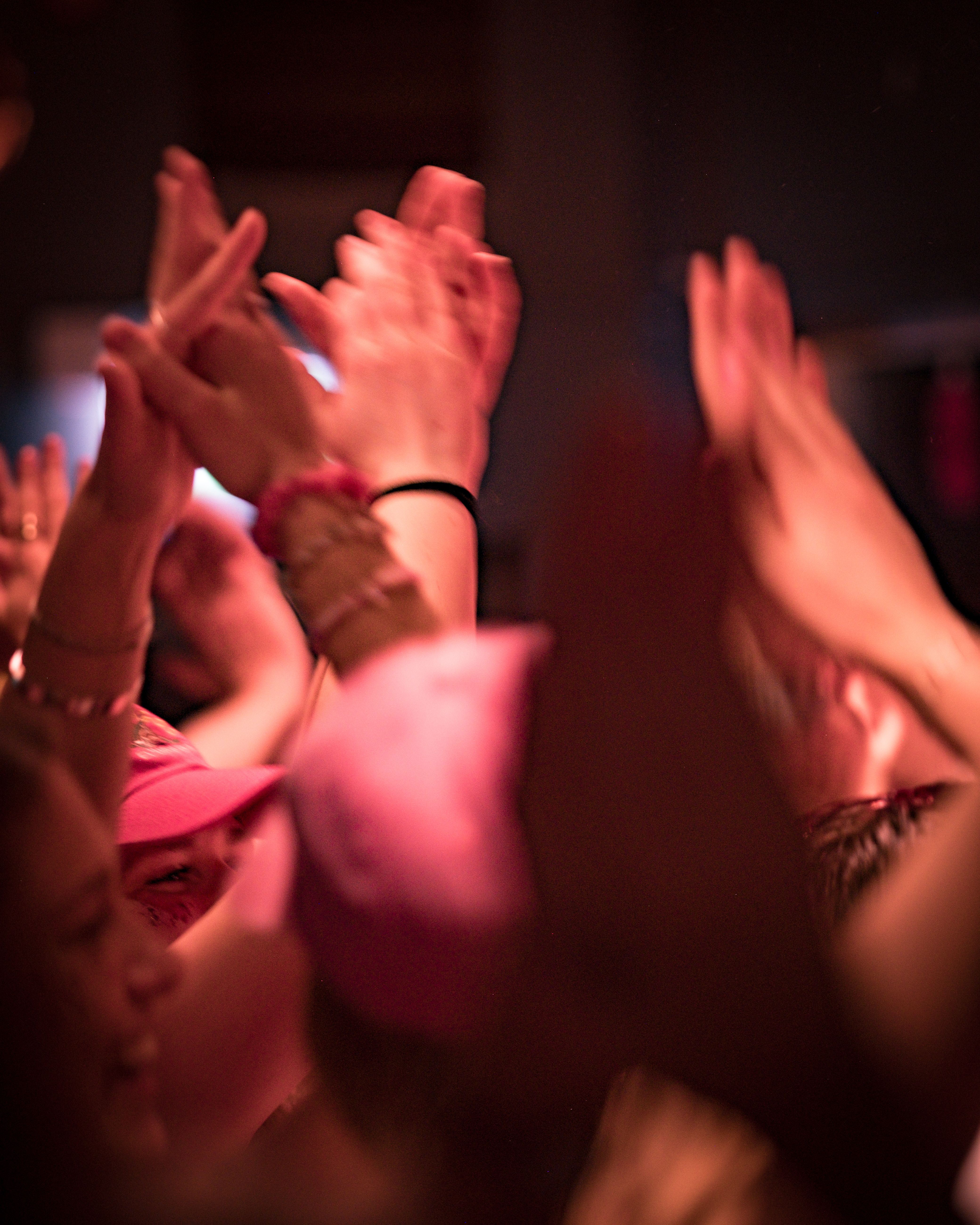 Blurred image of many hands clapping and raised in a dimly lit crowd.