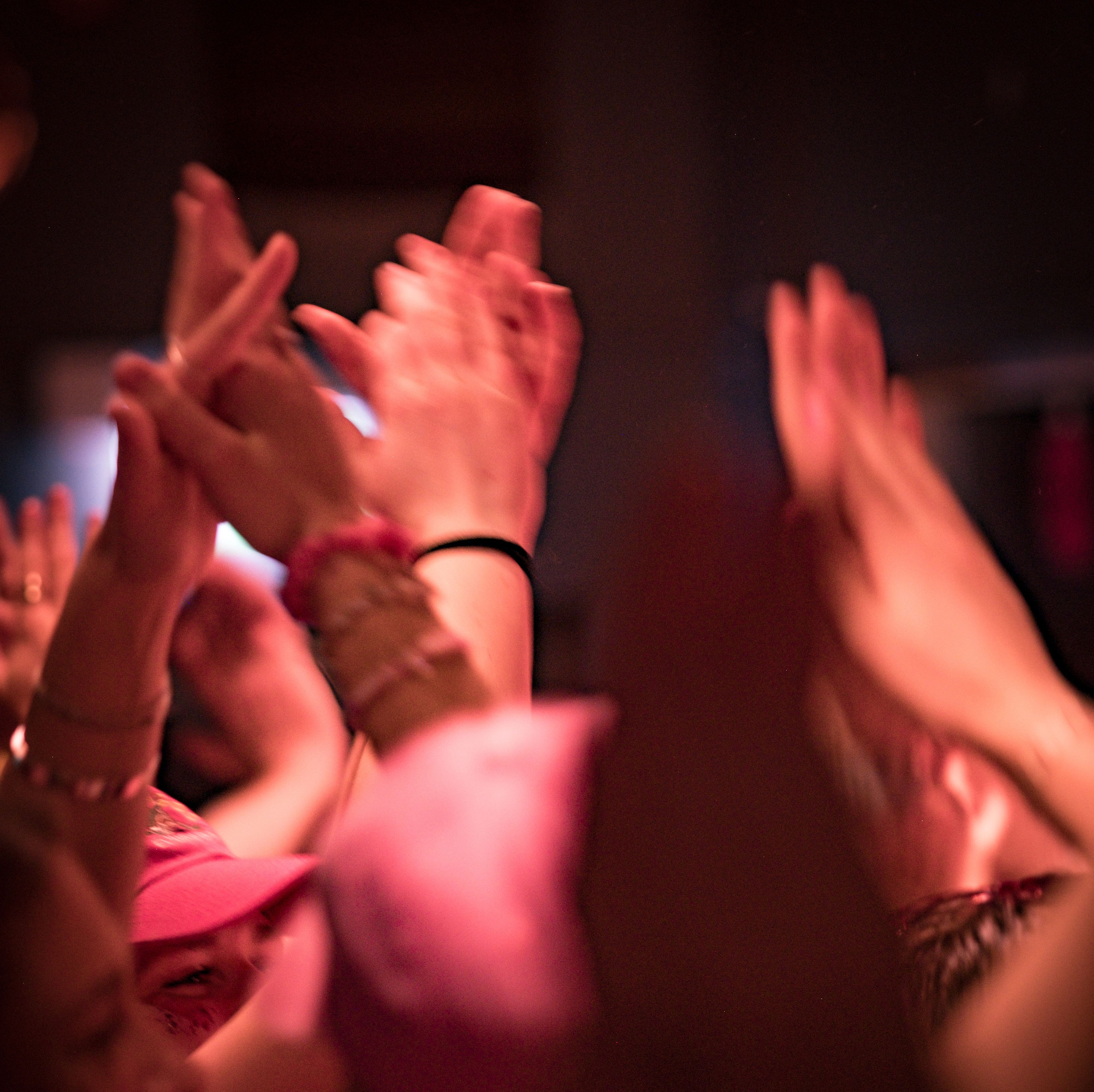 Blurred image of many hands clapping and raised in a dimly lit crowd.