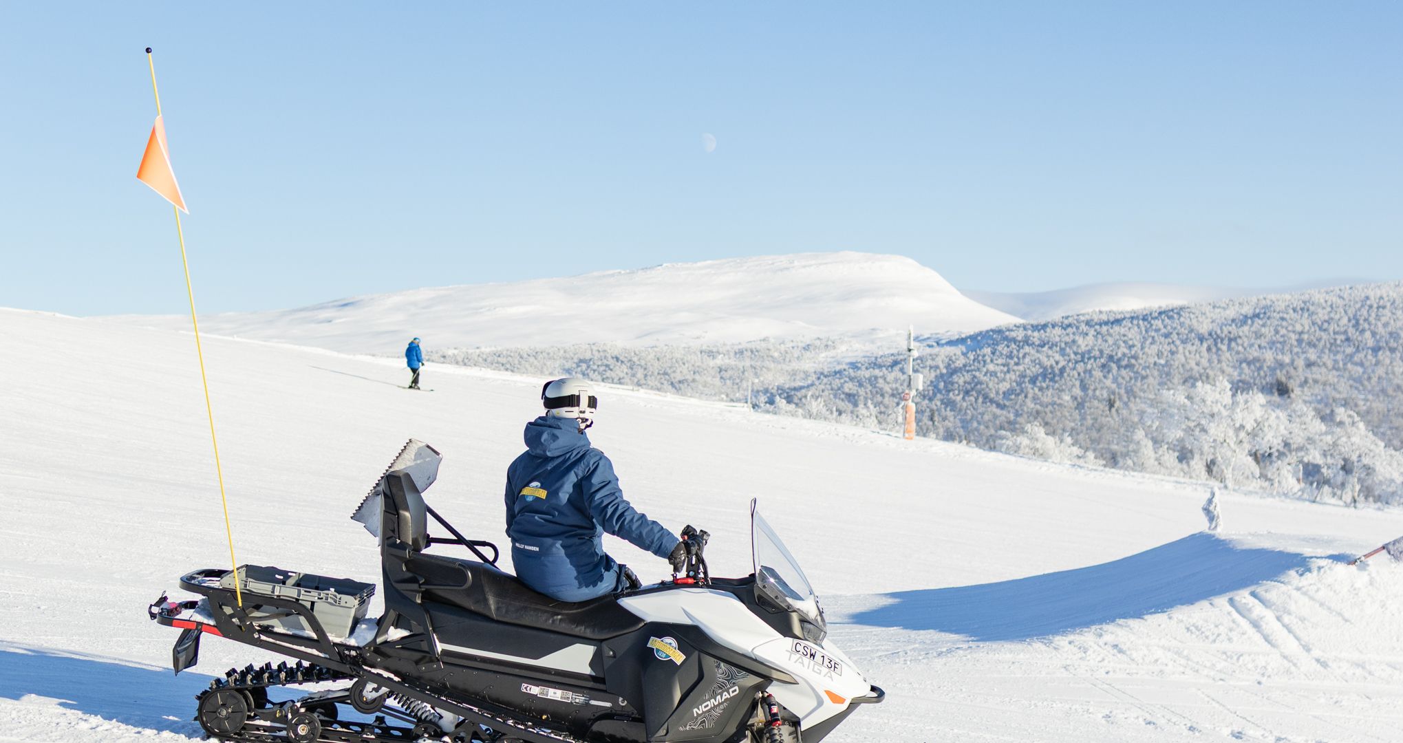 En kvinna som sitter på en snöskoter och tittar ut över en skidanläggning.