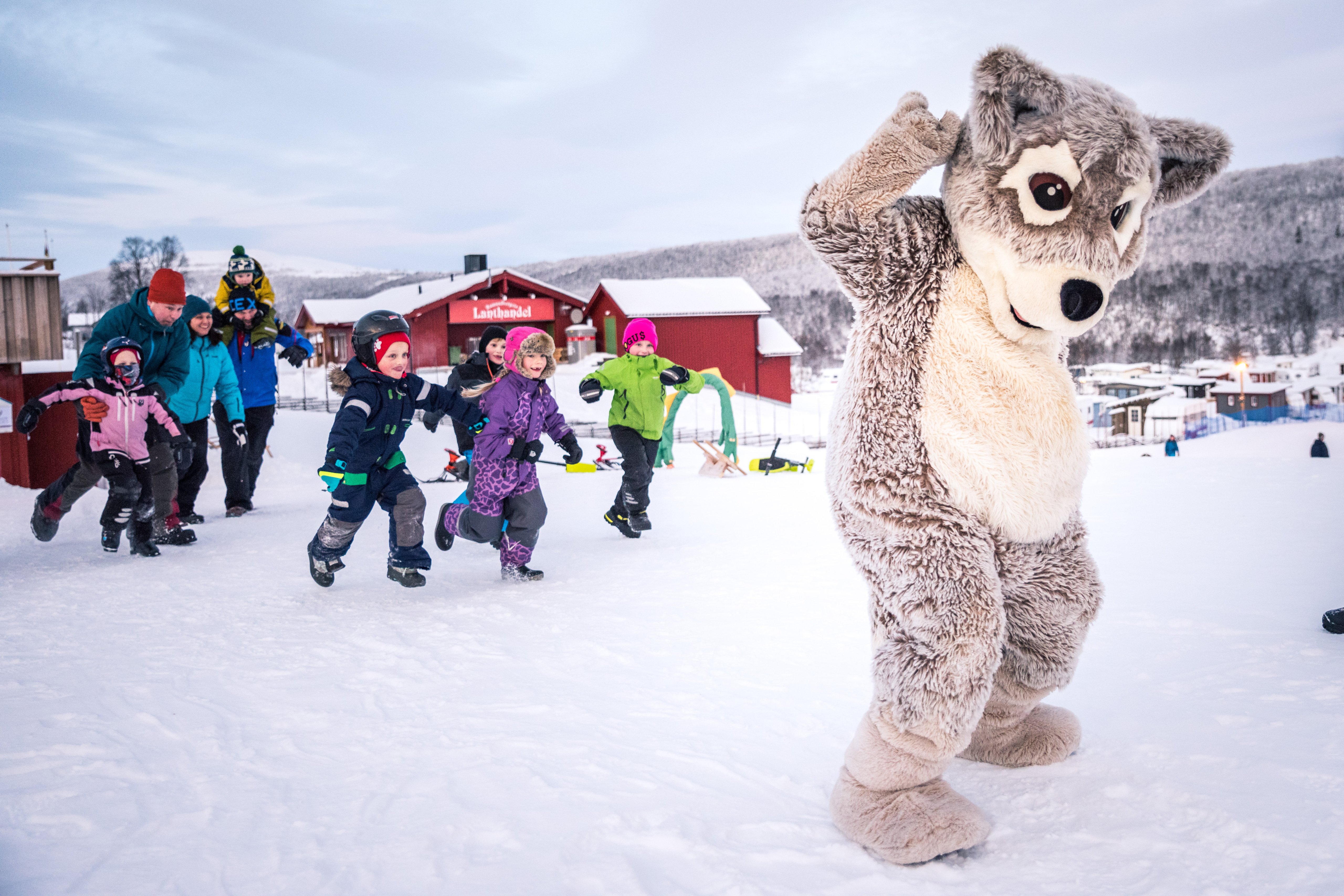 A group of children play in the snow with Mickelina the Arctic fox mascot.