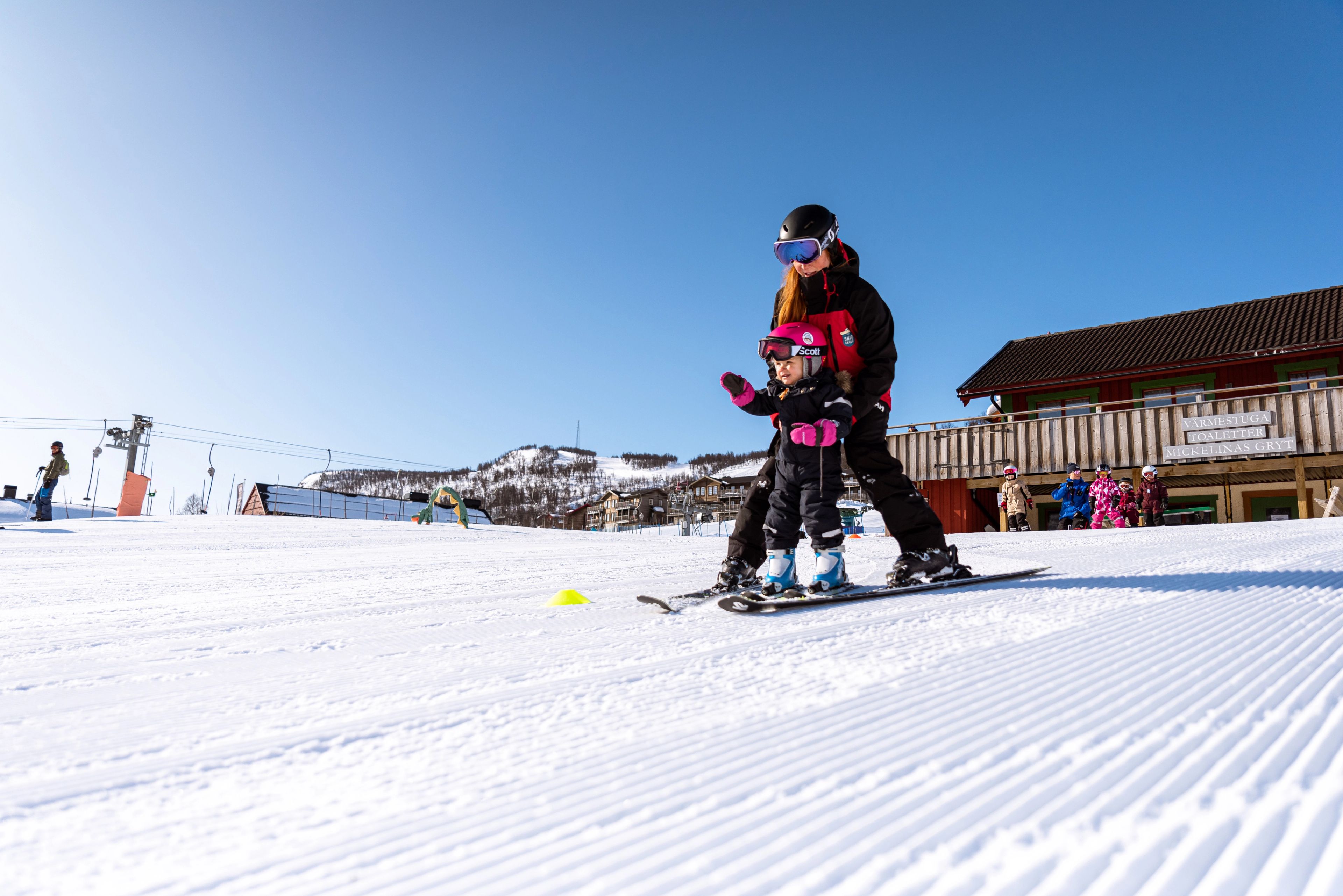 En skidlärare som lär ett barn åka skidor nedför en skidbacke.