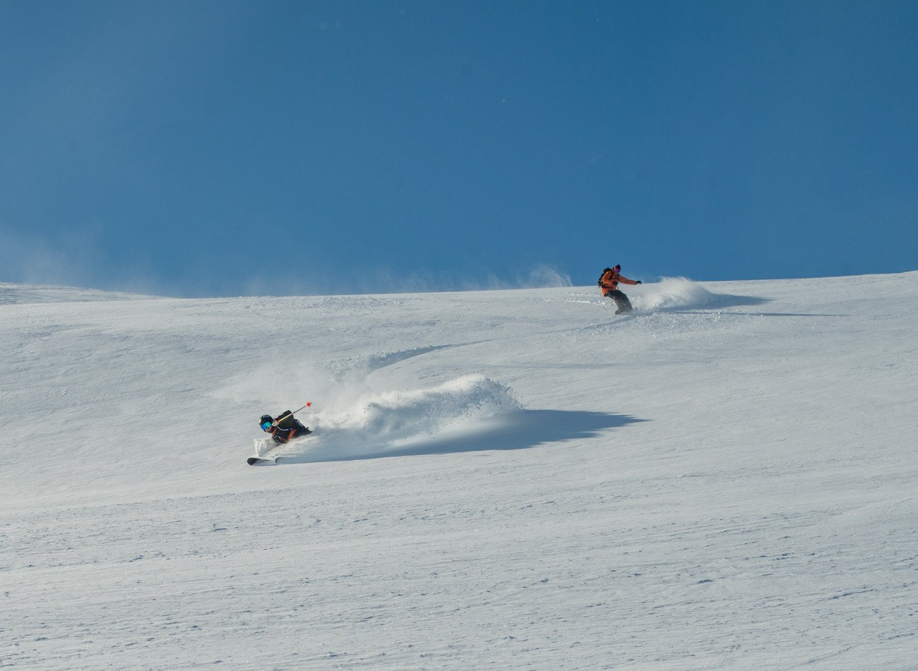 Two people skiing through powder down a snow-covered mountain.