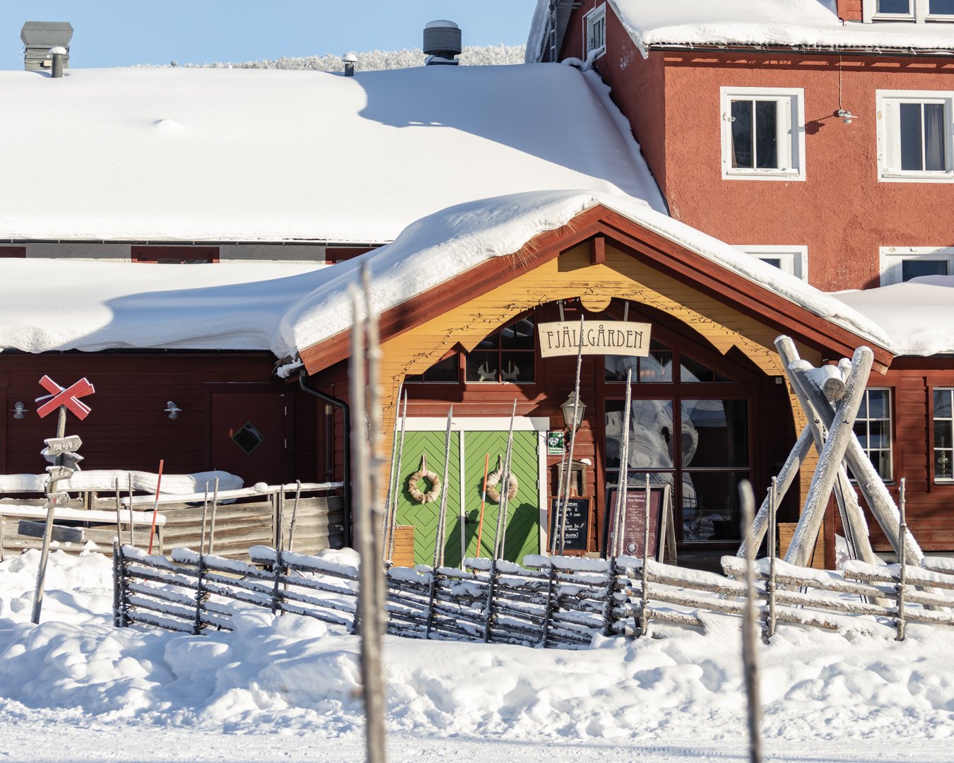 A snow-covered mountain hotel beside a traditional wooden fence.