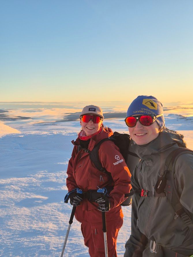 Två topptursguider som står på toppen av en snötäckt sluttning.