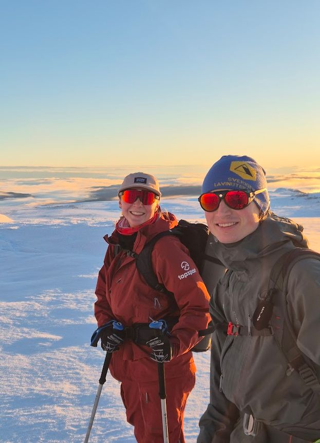 Två topptursguider som står på toppen av en snötäckt sluttning.
