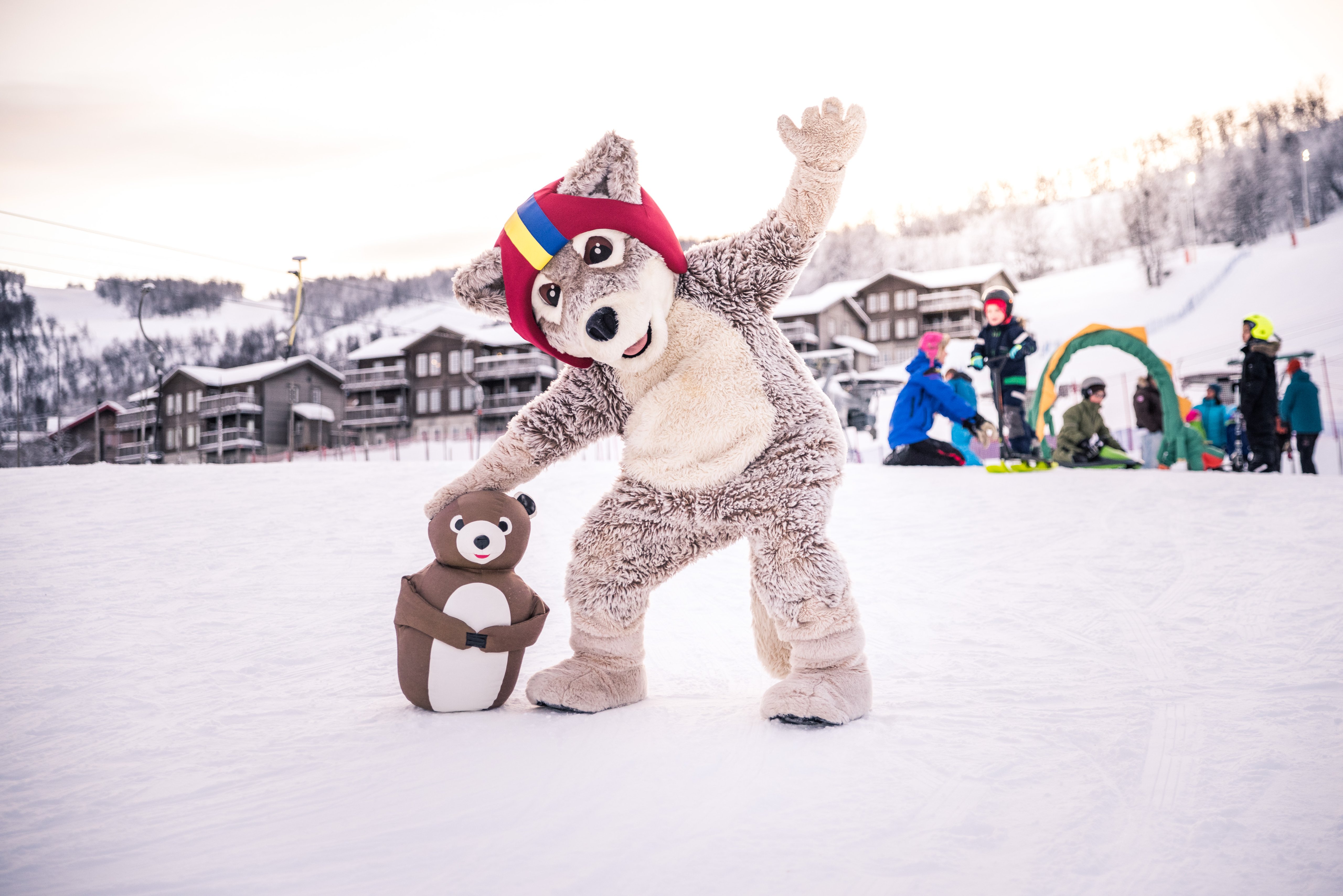 Mickelina the Arctic Fox, our mascot, stands in the snow and waves.