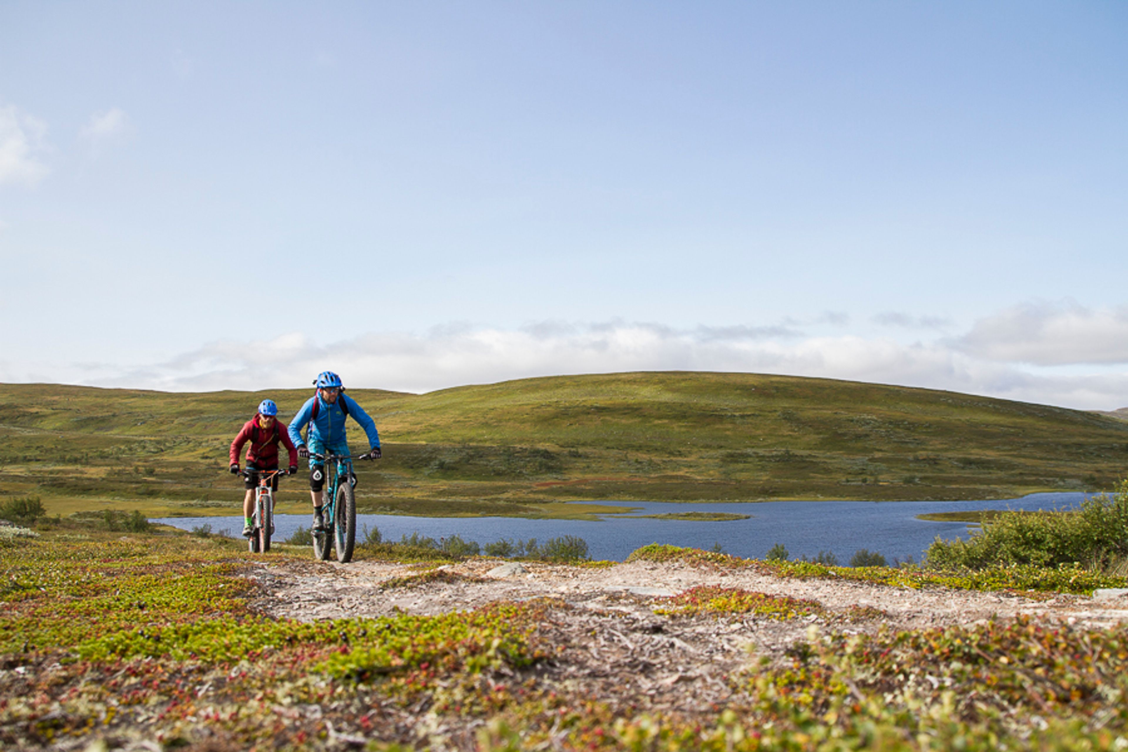 Några personer som cyklar på en stig på ett fjäll utmed en sjö
