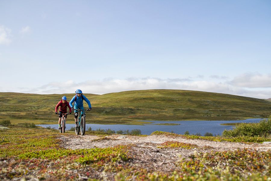 Några personer som cyklar på en stig på ett fjäll utmed en sjö