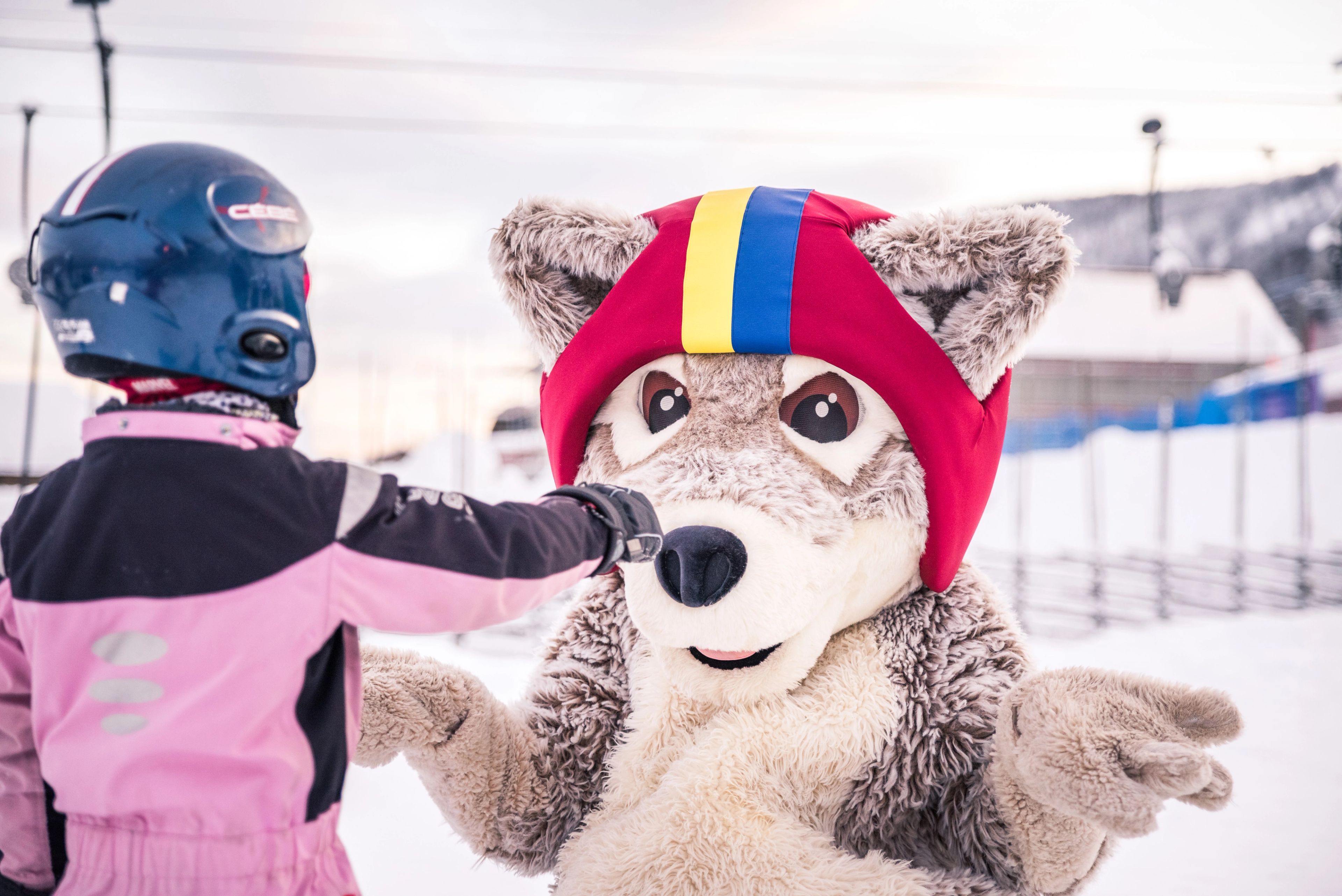 Maskoten Mickelina Fjällräv leker med ett barn i snön.