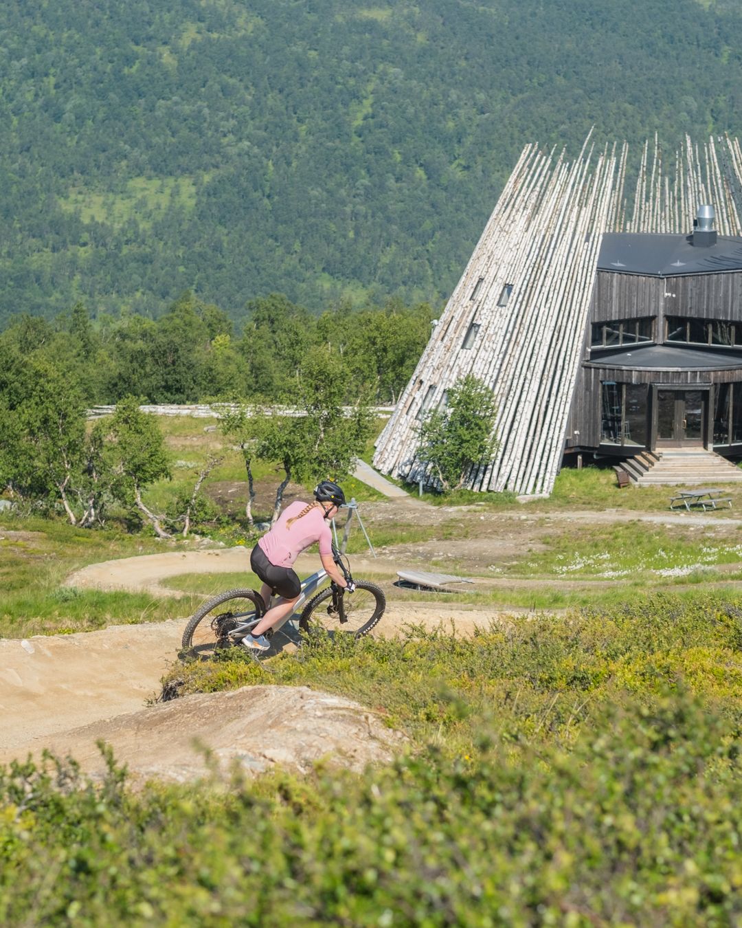 En kvinna cyklande på en flowtrail mot en modern byggnad.