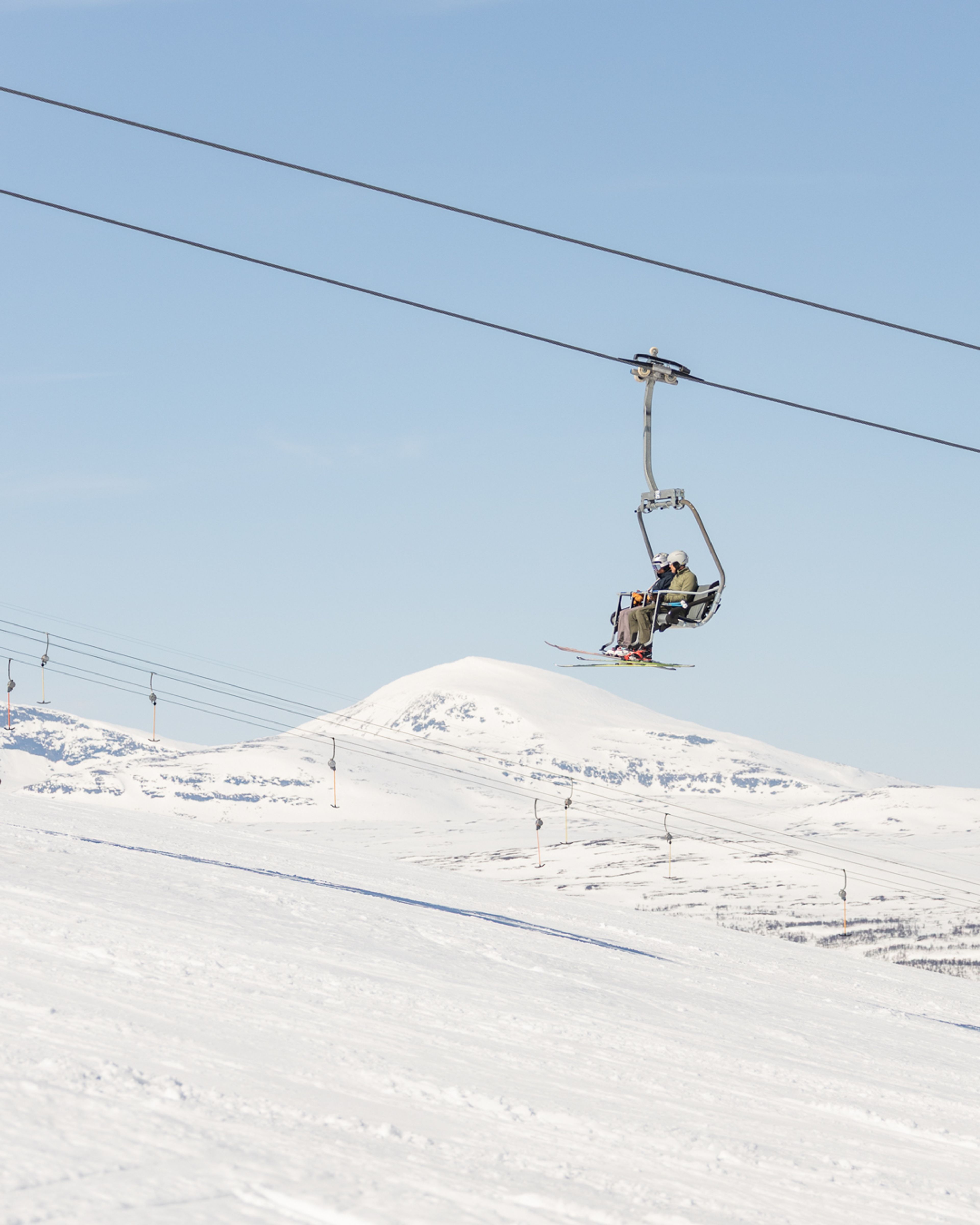 Två personer som åker skidlift uppför en snötäckt bergssluttning.