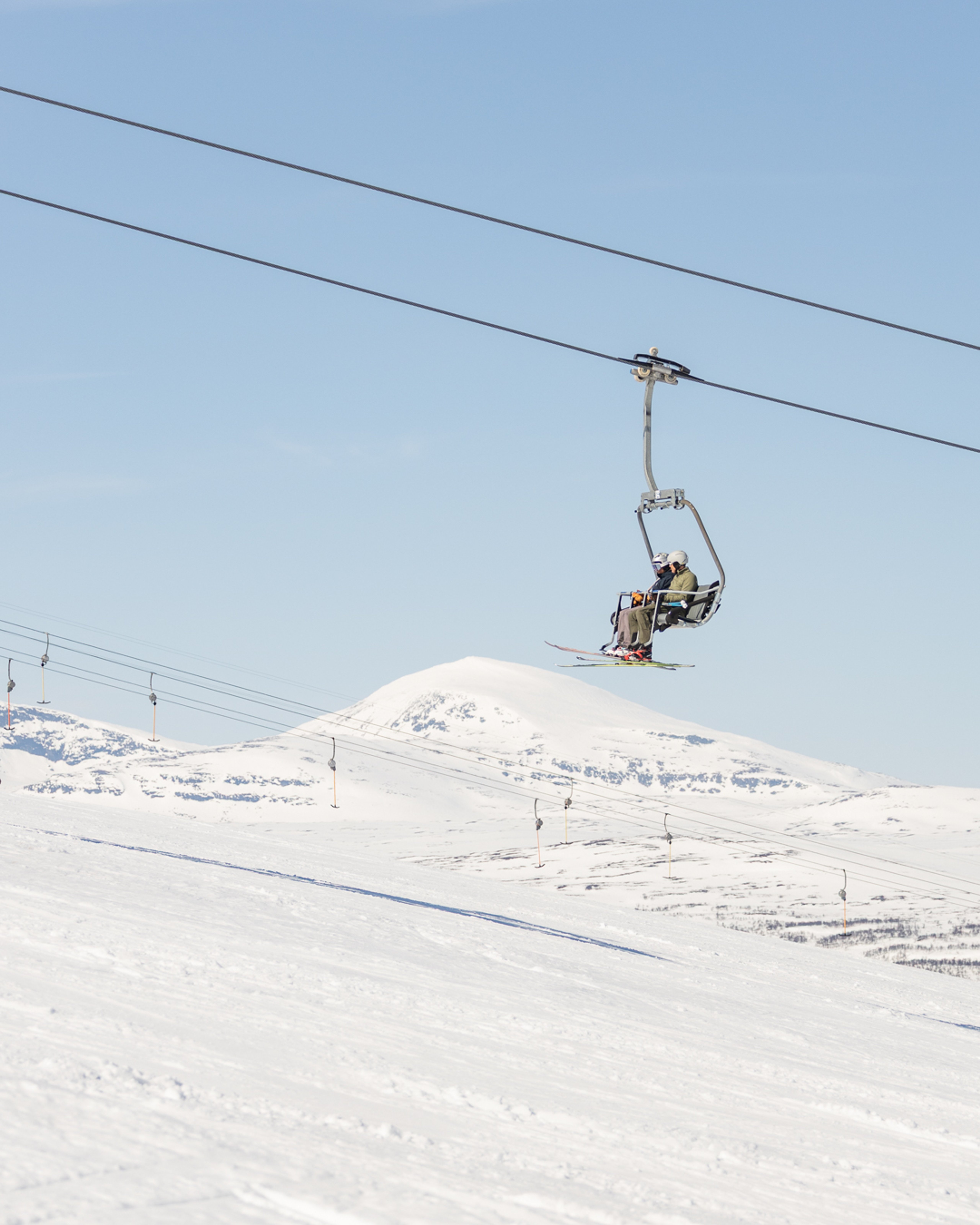 Två personer som åker skidlift uppför en snötäckt bergssluttning.