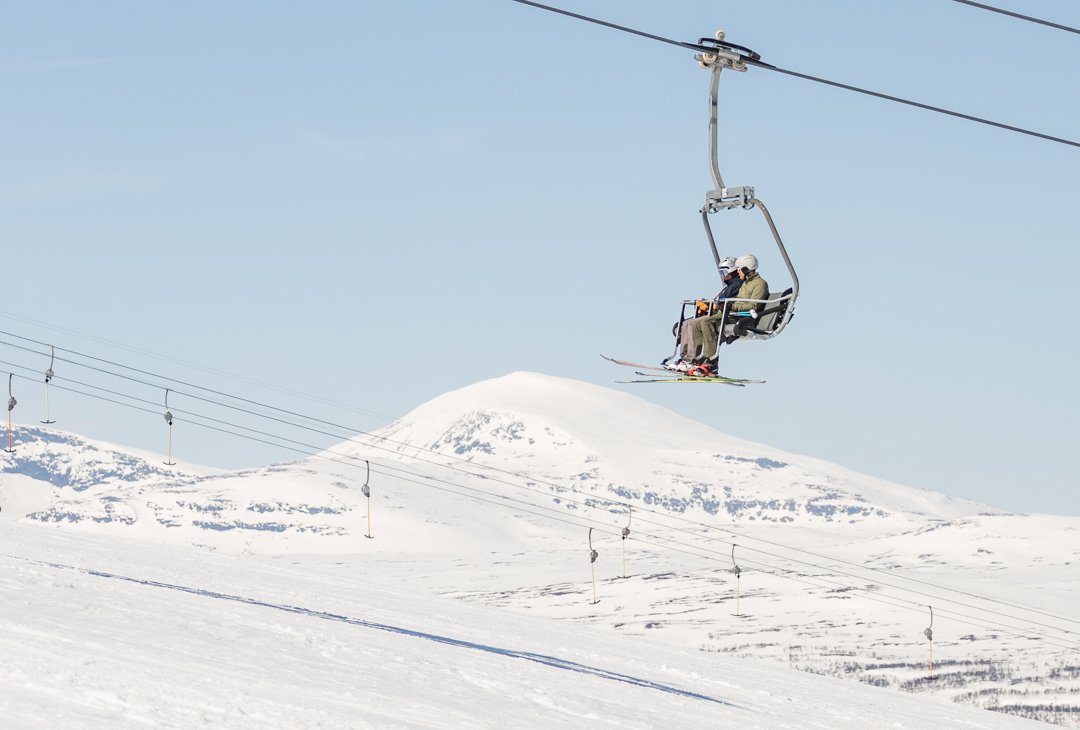 Two people riding a ski lift up a snow-covered mountainside.