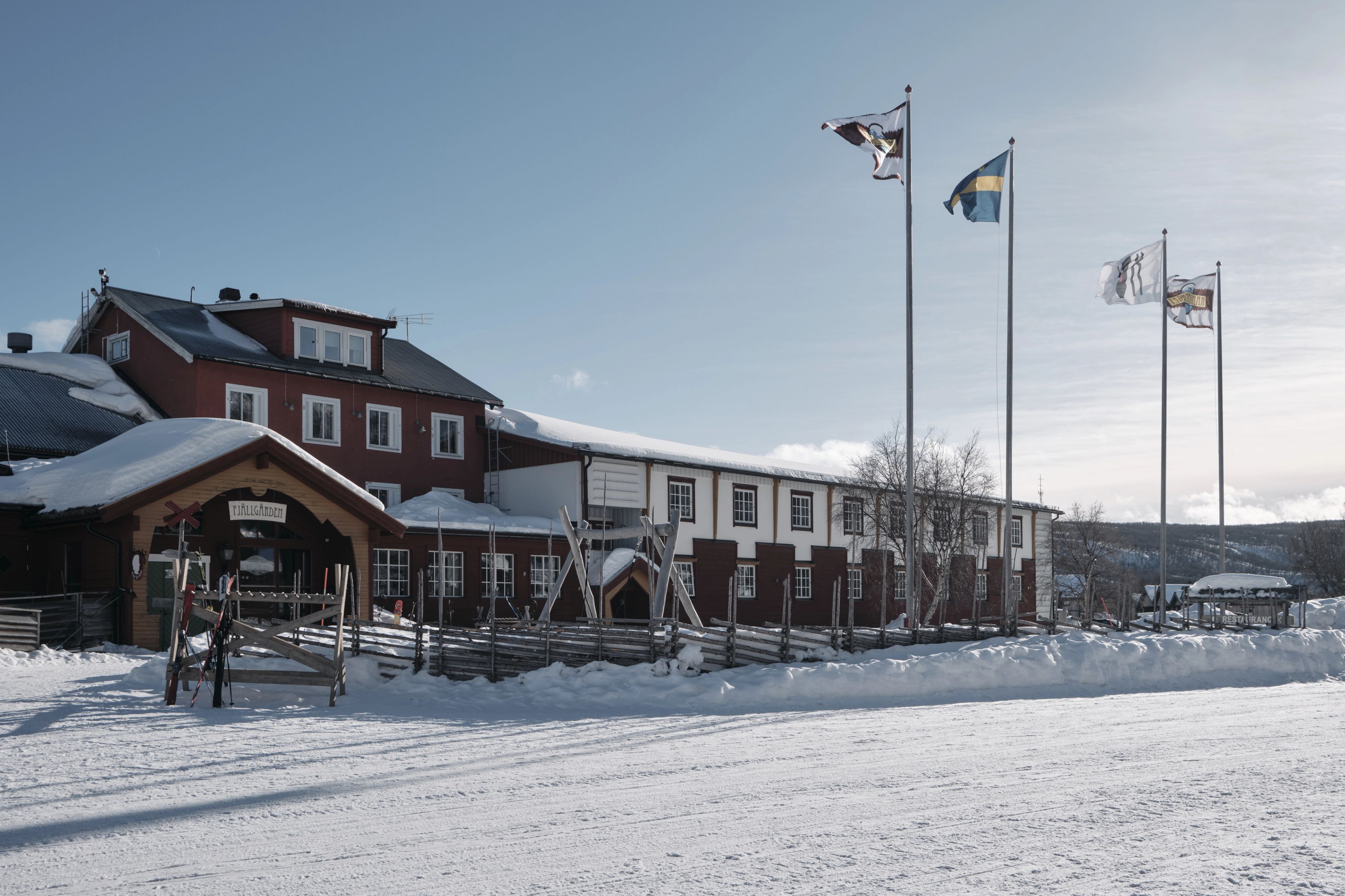 En röd hotellbyggnad i trä med gärdesgårdar framför och flaggor i motsol.