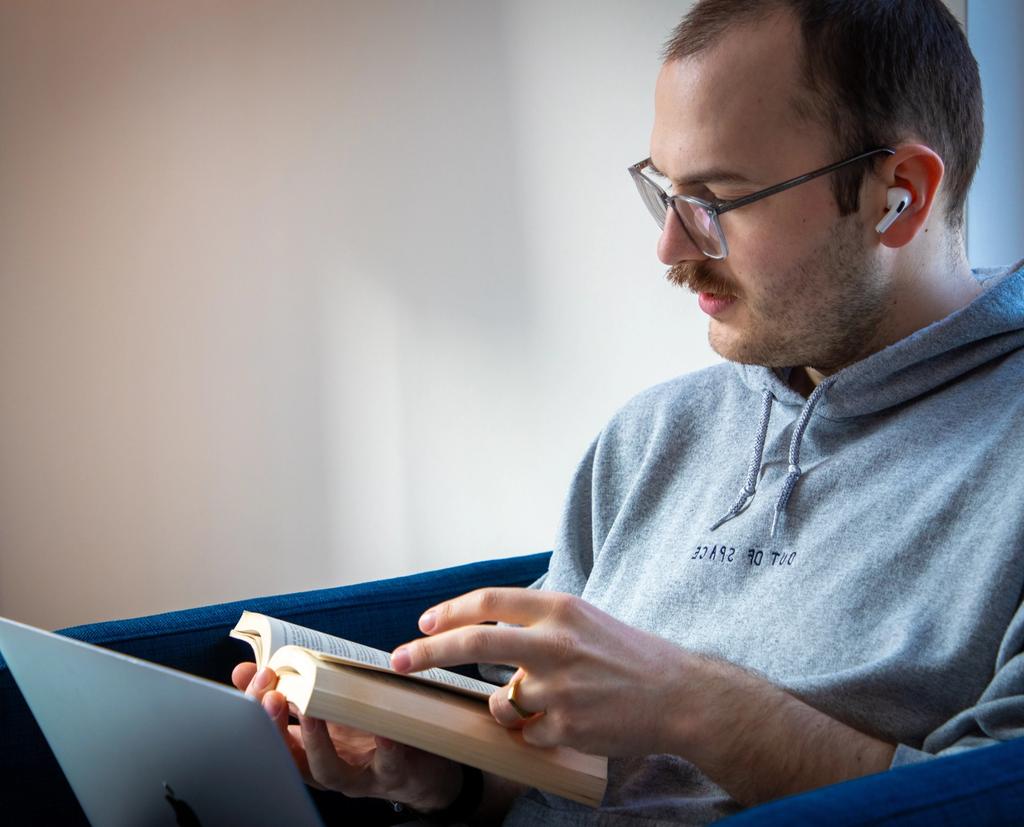 Student mit Brille und Kopfhörern lernt konzentriert mit Buch und Laptop