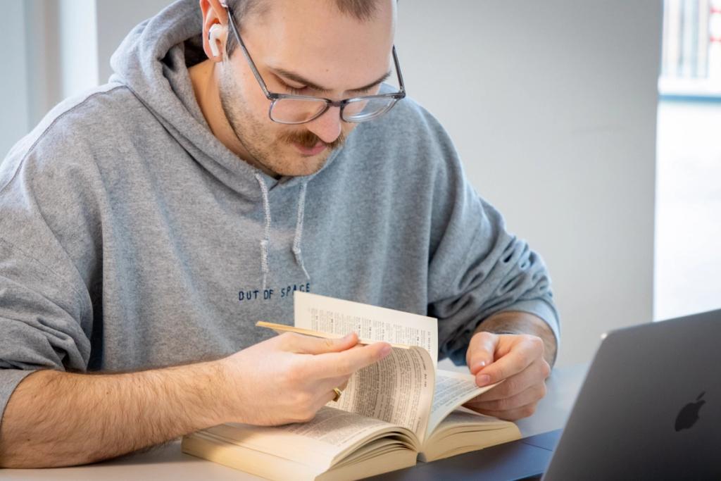 Student lernt konzentriert mit Jura-Lehrbuch vor offenem Laptop