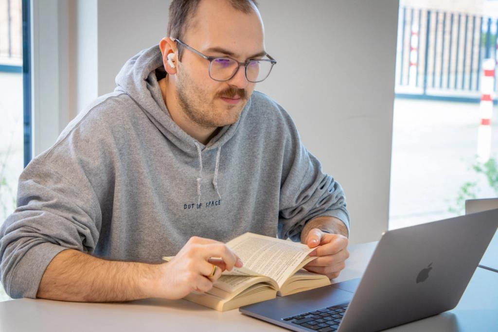 Jura-Student sitzt mit aufgeschlagenem Lehrbuch und starrt auf seinen Laptop