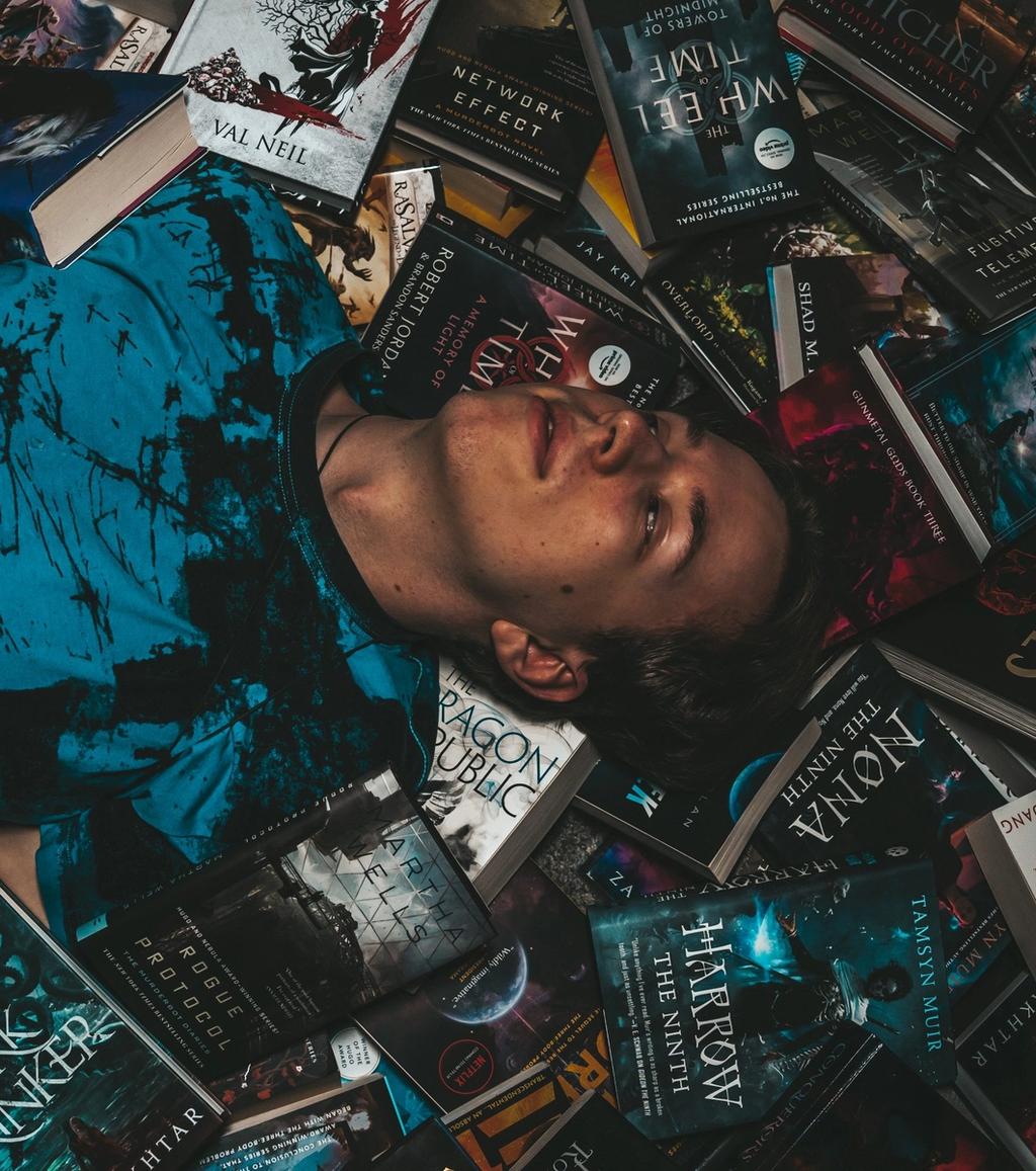 Sinan, Jurakompakt-Mitgründer, lächelnd auf Büchern liegend in blauem Shirt