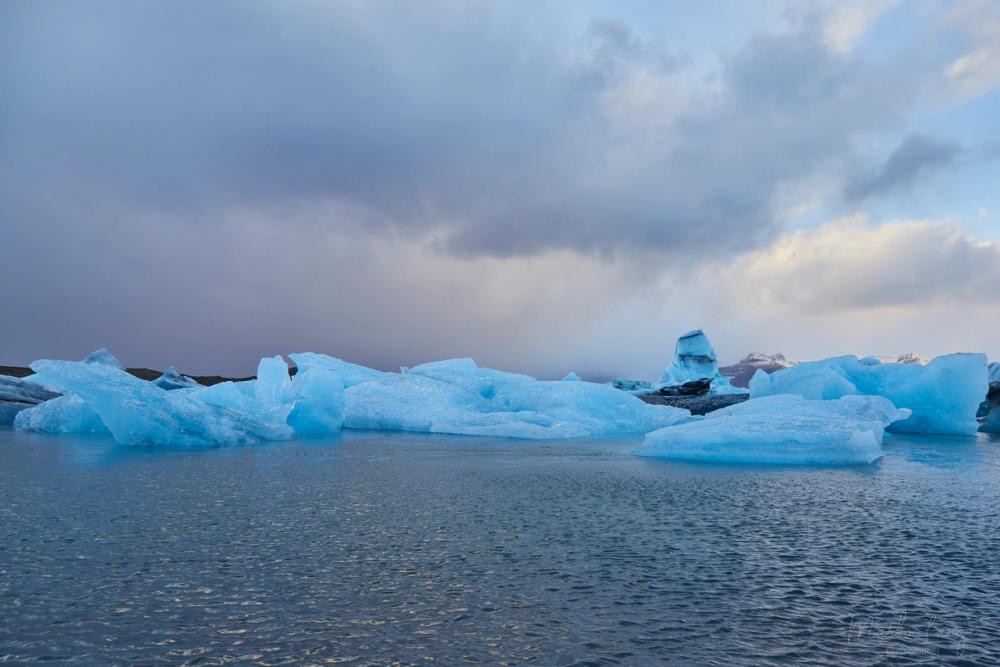 Weit verstreute Eisberge auf dem Jökulsárlón unter dramatischem Abendhimmel.
