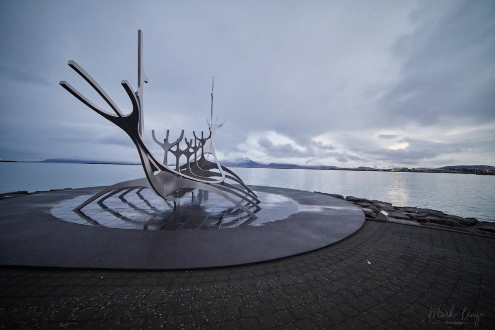 Die stählerne Wikingerschiff-Skulptur Sólfar steht am Ufer, dahinter die ruhige Bucht und der schneebedeckte Esja unter grauem Himmel.
