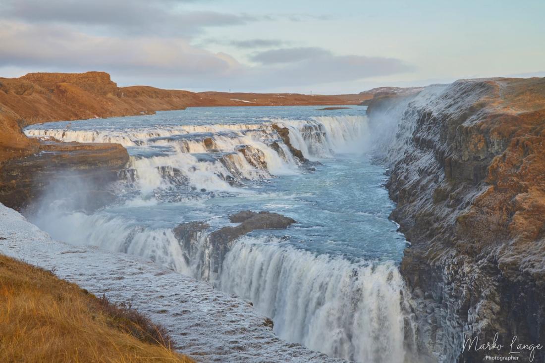 Der zweistufige Wasserfall Gullfoss stürzt über breite Felsstufen in eine tiefe Schlucht, Gischt steigt auf.