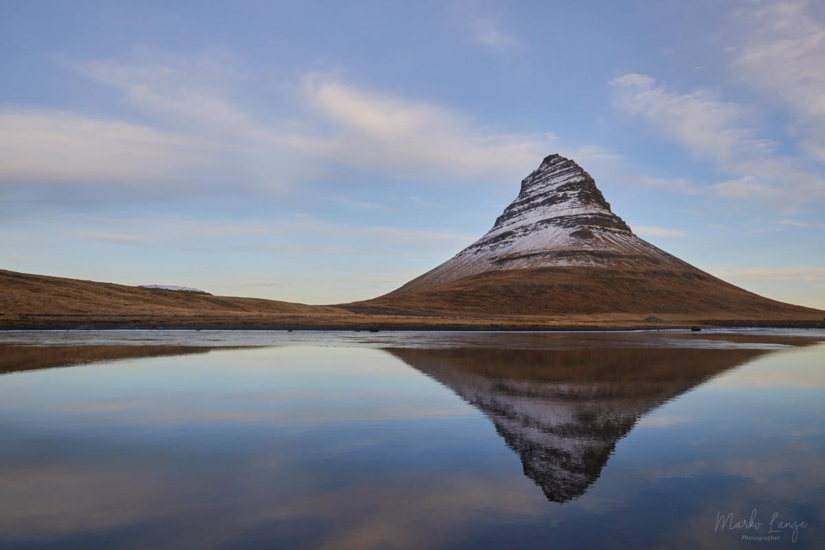 Der Kirkjufell spiegelt sich als unverwechselbare Silhouette in ruhigem Wasser.