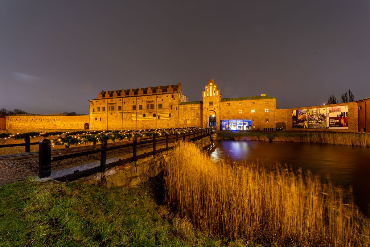 Die alte Backsteinfestung Malmöhus liegt nachts hell erleuchtet hinter ihrem Wassergraben.