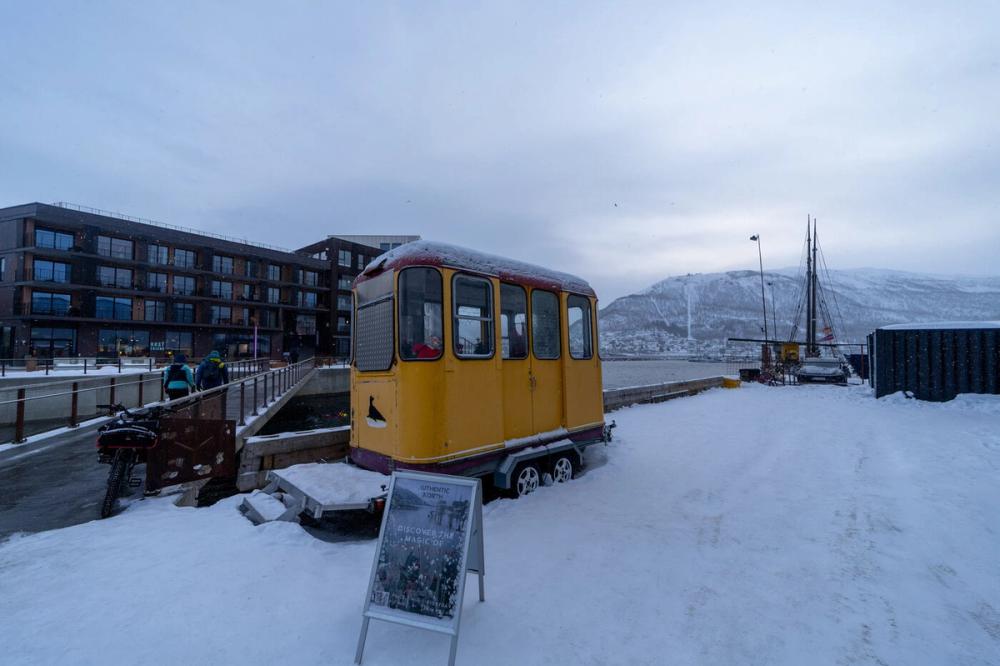 Nachgebaute historische Straßenbahn als Touristen-Attraktion am winterlichen Hafen von Tromsø, im Hintergrund der Berg Fjellheisen.